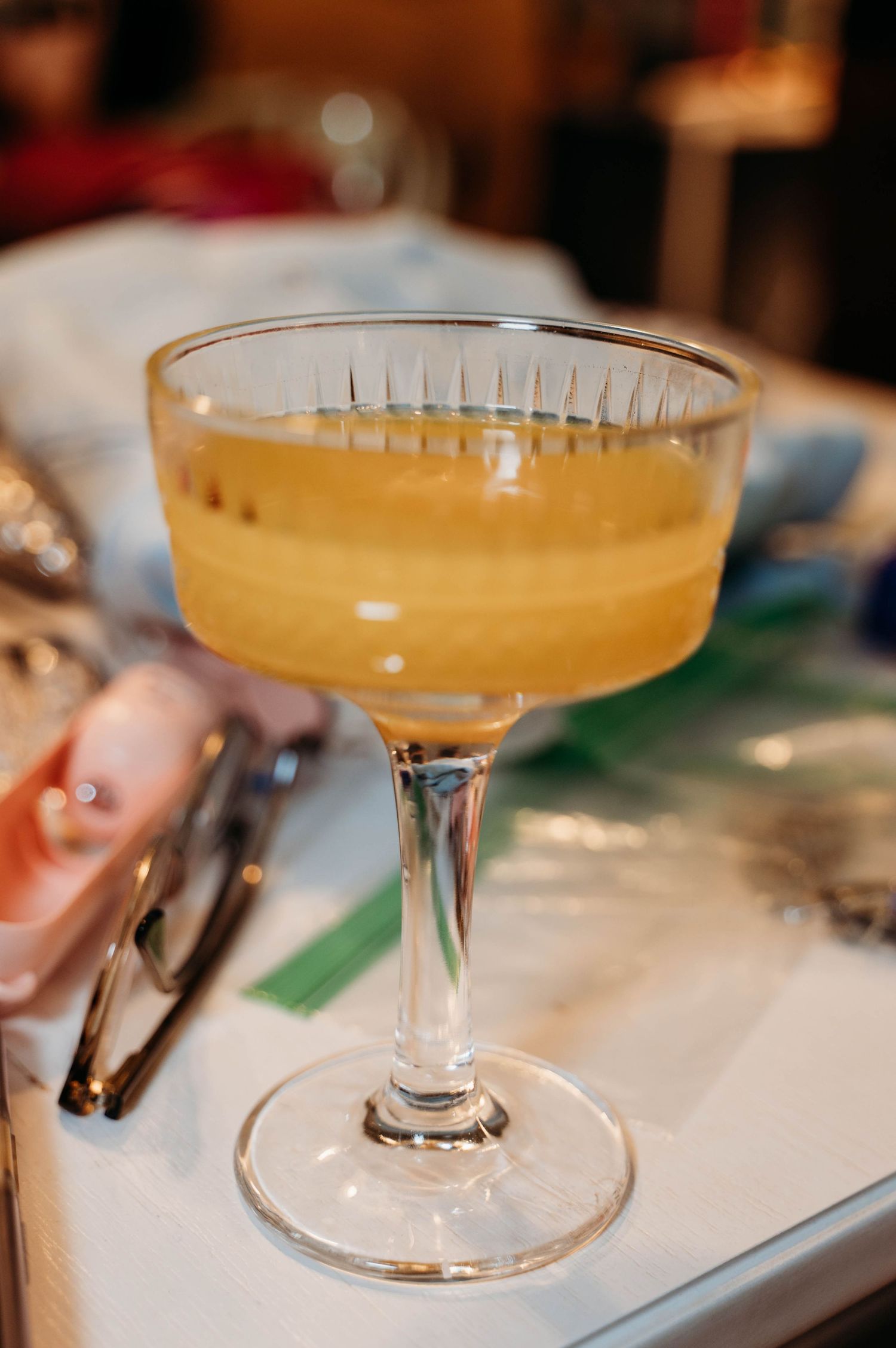 A sequence of cocktail glasses filled with golden-colored drinks sitting on a white surface, shown from different angles.