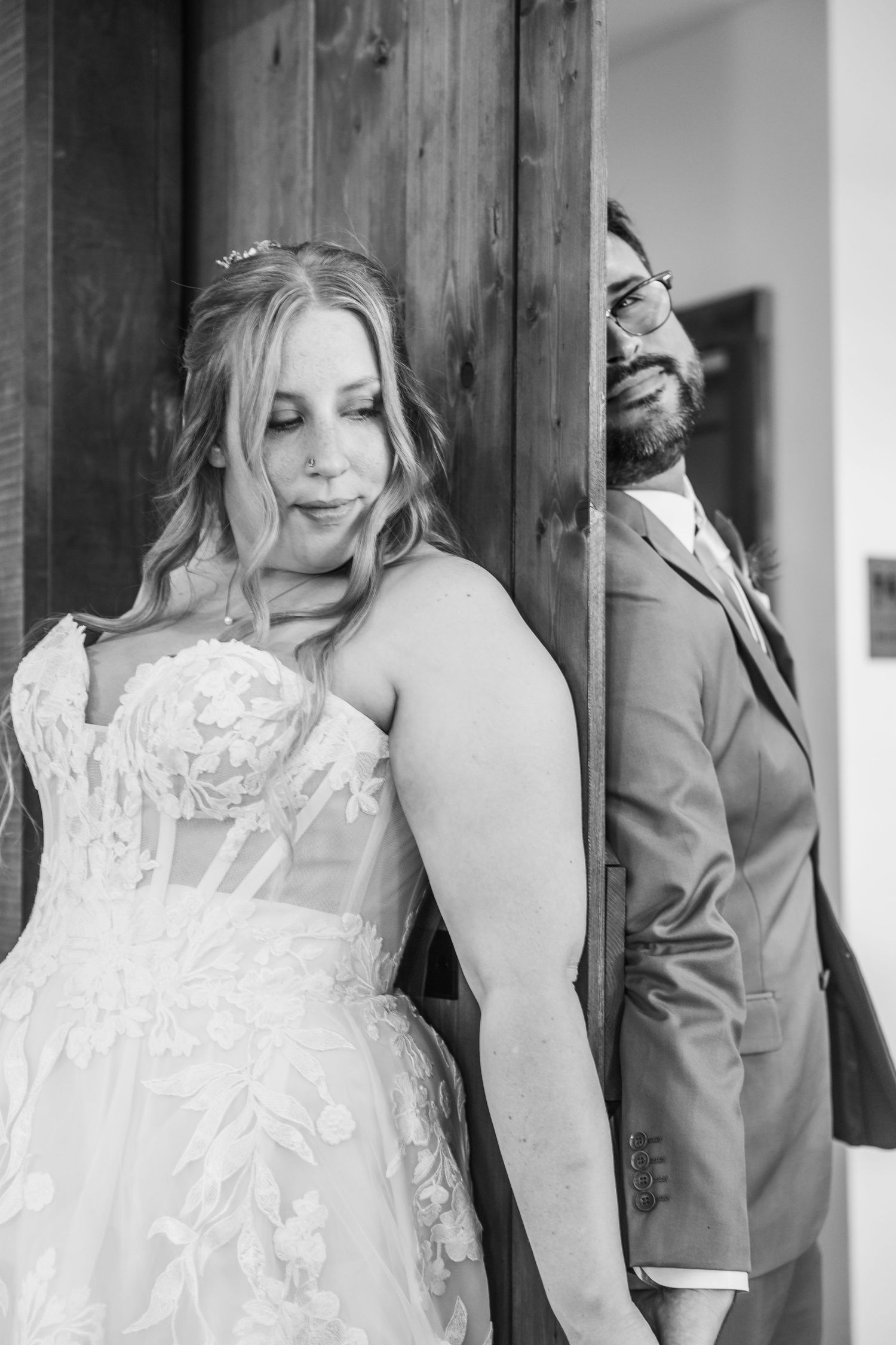 Black and white wedding photo showing a couple playfully posing on opposite sides of a wooden door.
