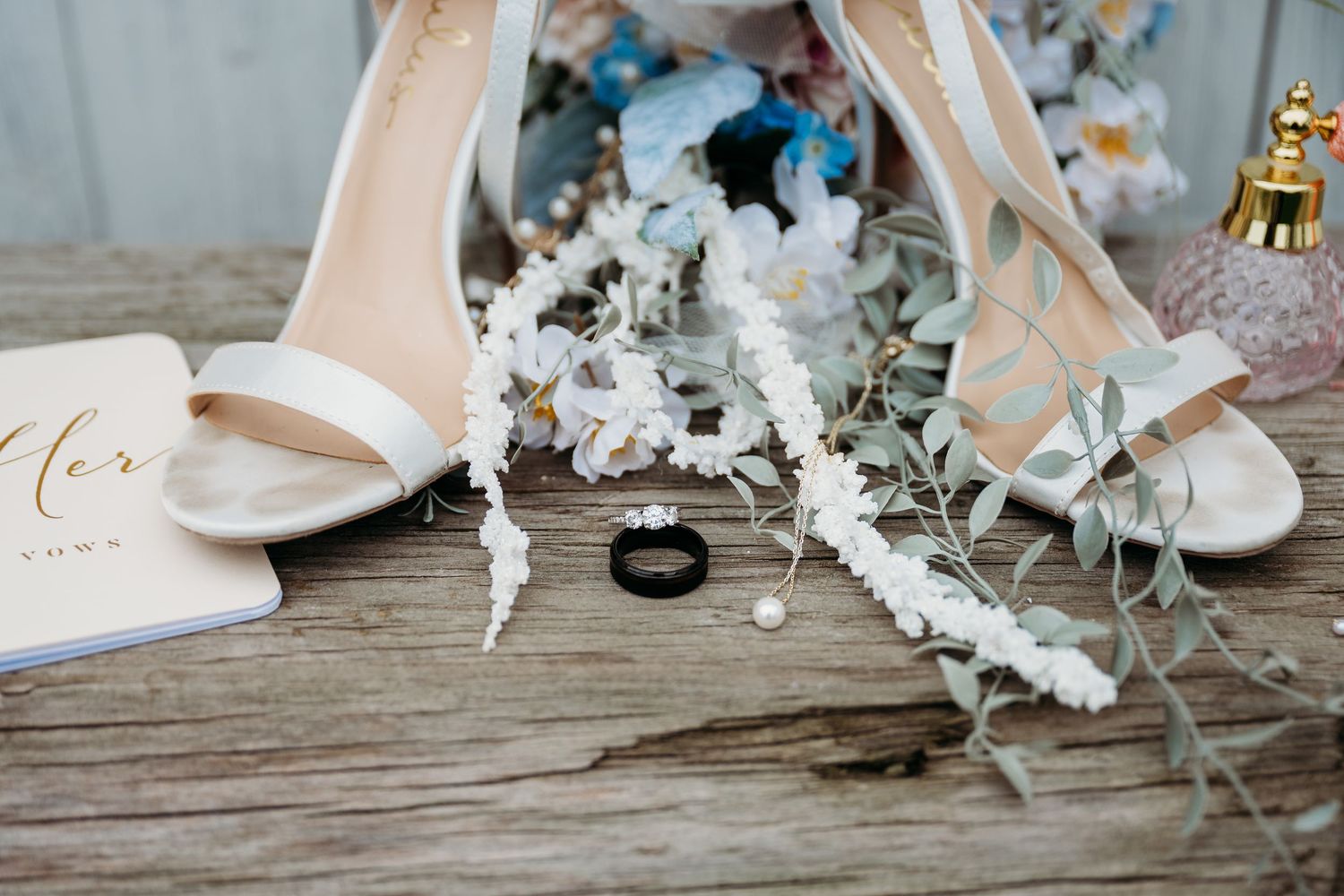 Wedding details featuring white bridal shoes, delicate floral arrangements, and wedding rings on rustic wooden surfaces.