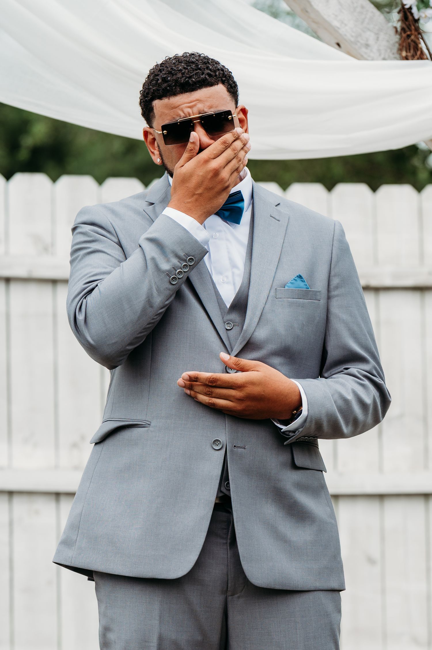Groomsmen in gray suits share an emotional moment at an outdoor wedding.
