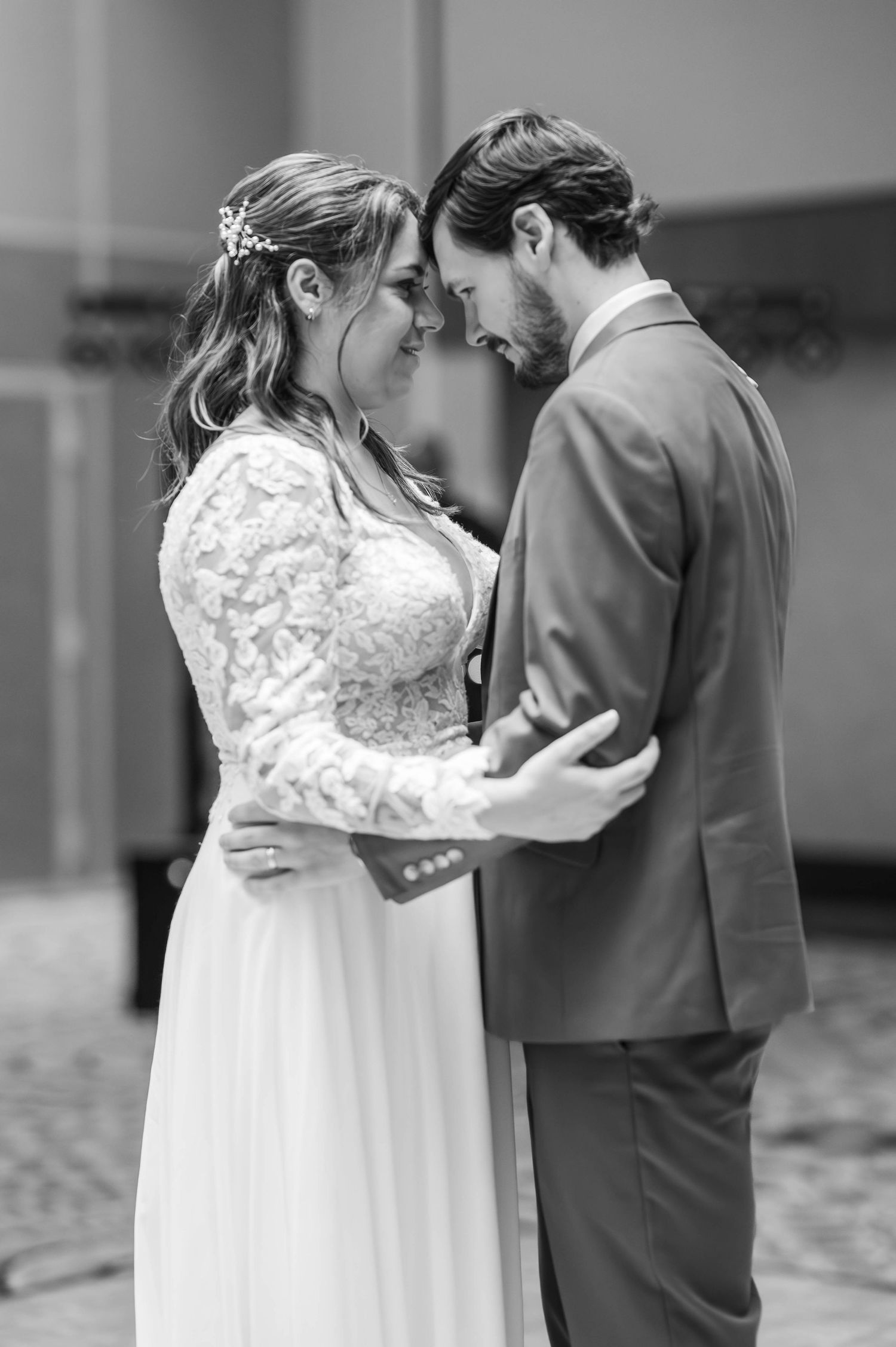 Black and white wedding portrait showing tender moment between couple in elegant attire.
