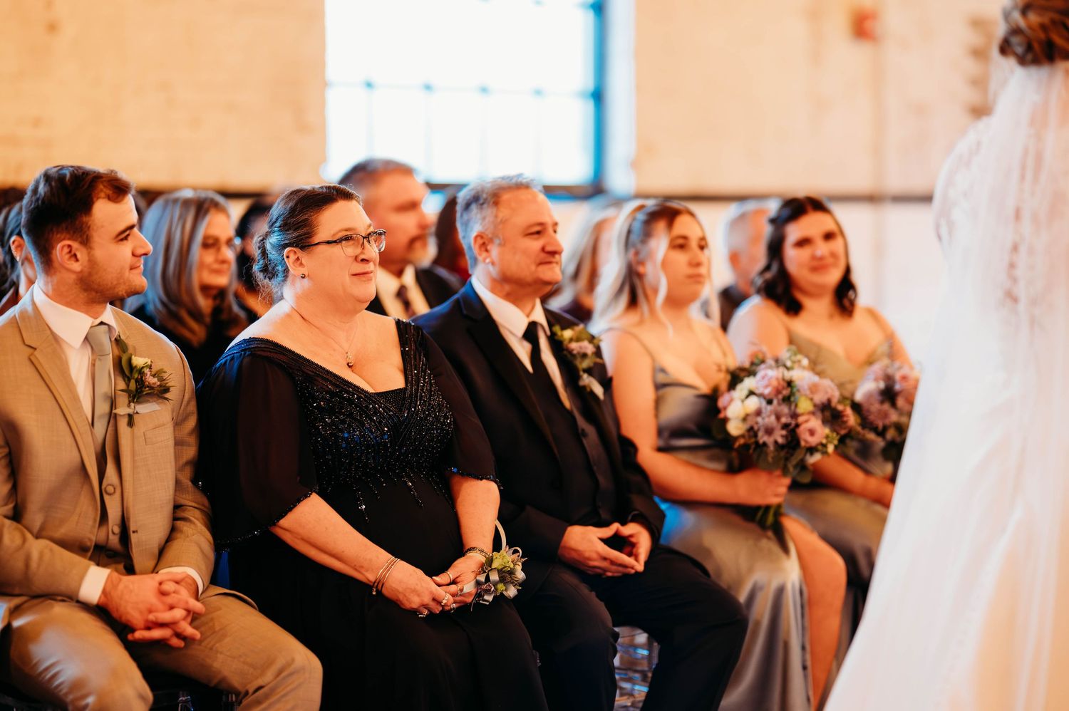 Wedding ceremony attendees watch emotionally from the front row during an indoor celebration.