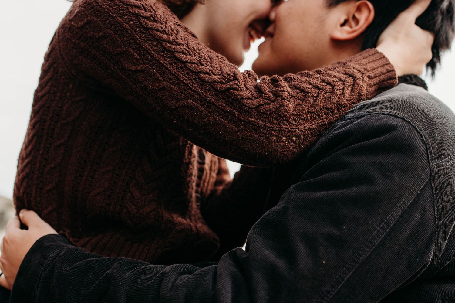 A close-up shot of two people embracing, one wearing a brown knit sweater and the other in black.