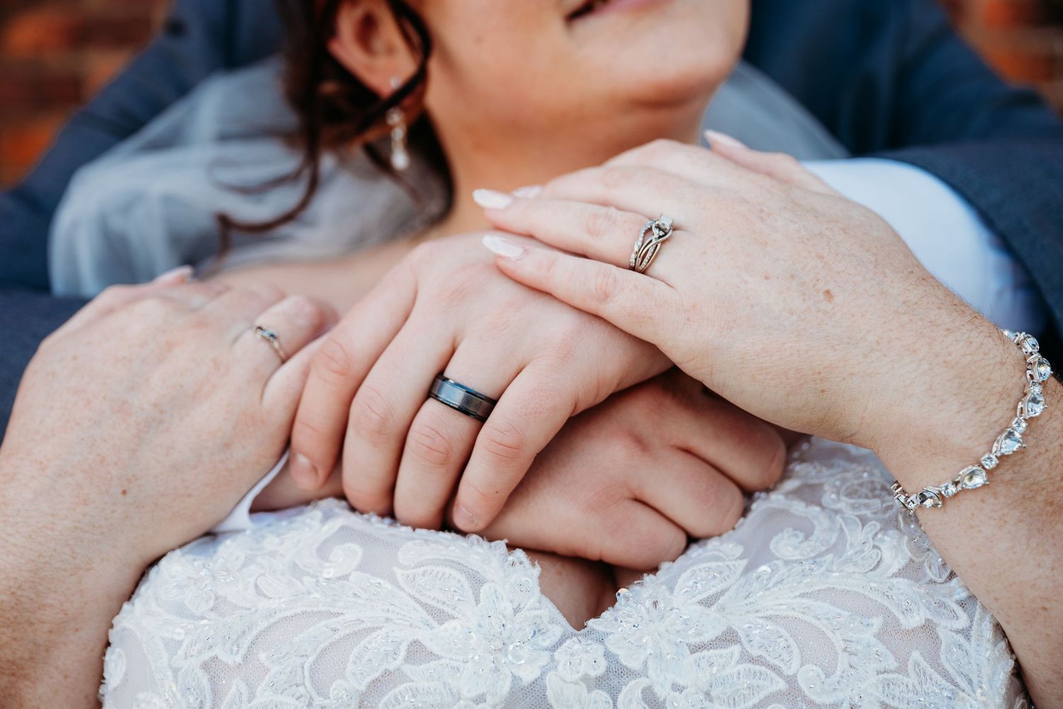 Close up shot of newlywed hands showing wedding rings against white lace bridal dress fabric.