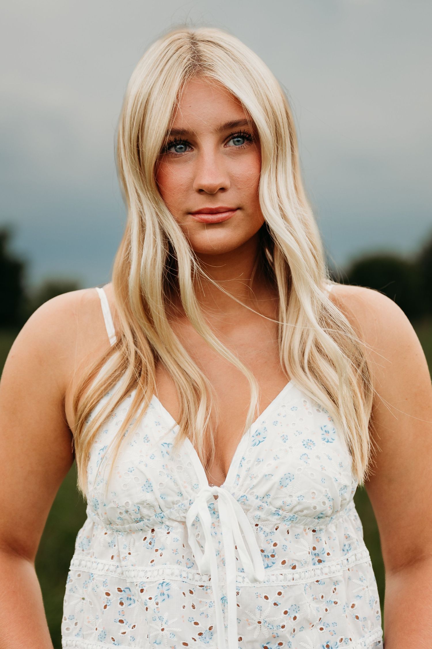 Portrait with blonde hair and white lace top in natural outdoor setting.