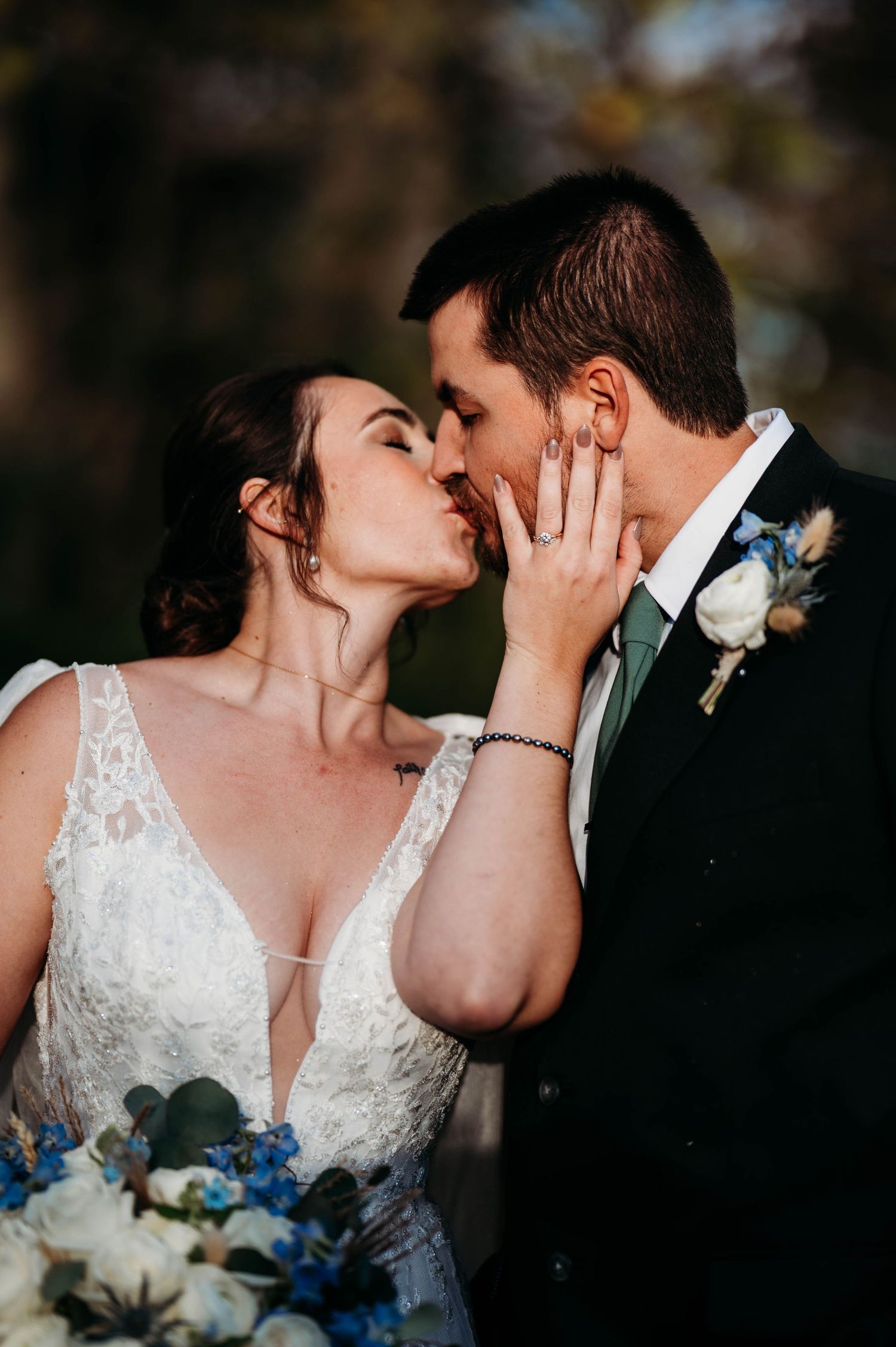 A romantic wedding moment captured as a couple shares a tender kiss while holding a blue and white floral bouquet.