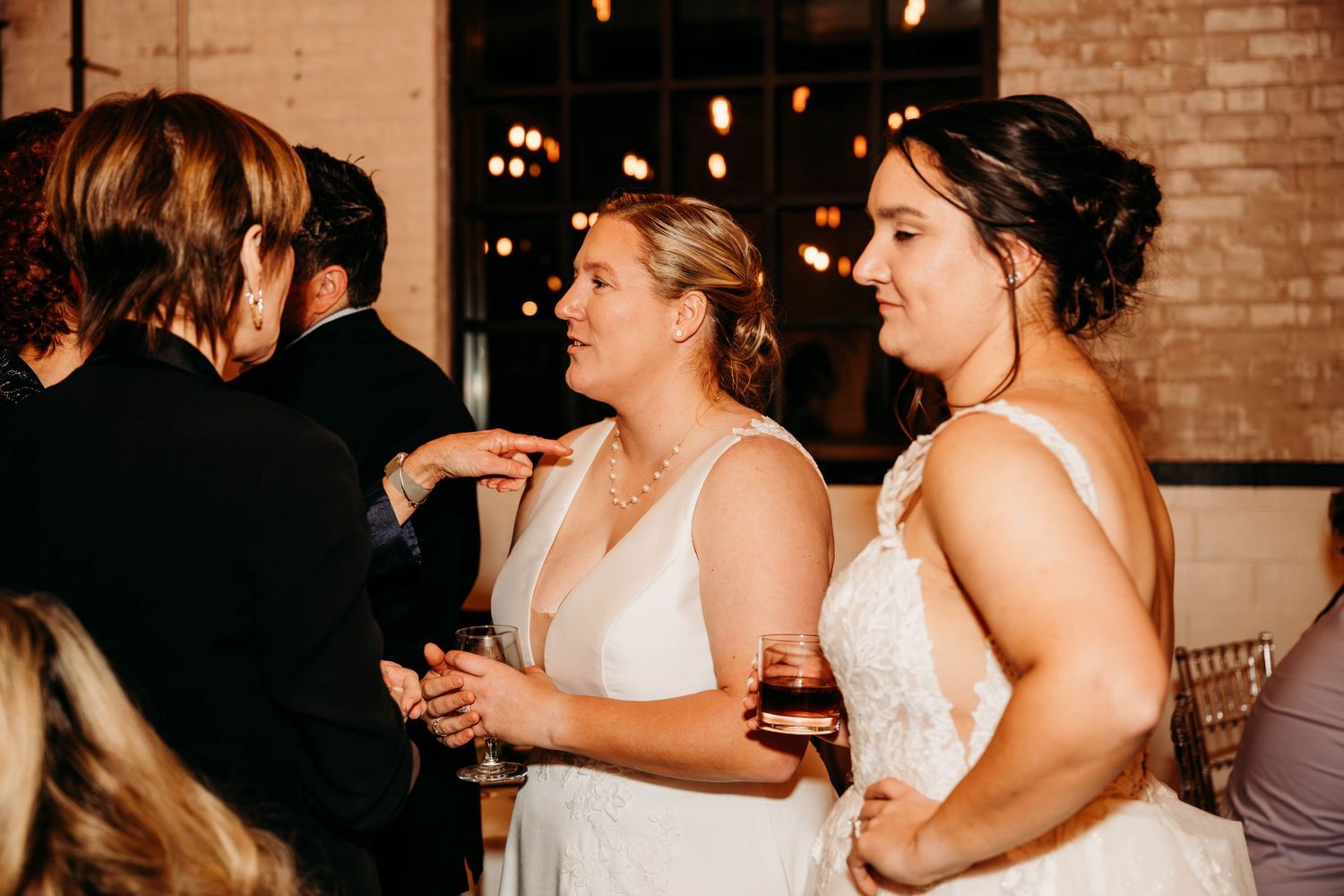 A group of people dancing and celebrating at a wedding reception in a rustic brick-walled venue with warm lighting.