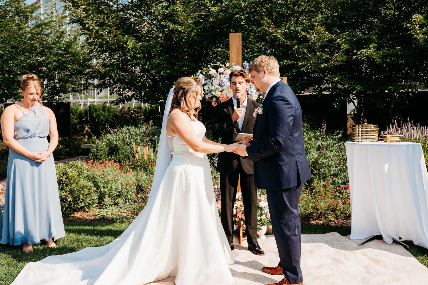 Bride and groom exchange vows outdoors at an elegant garden wedding ceremony with floral arch backdrop.