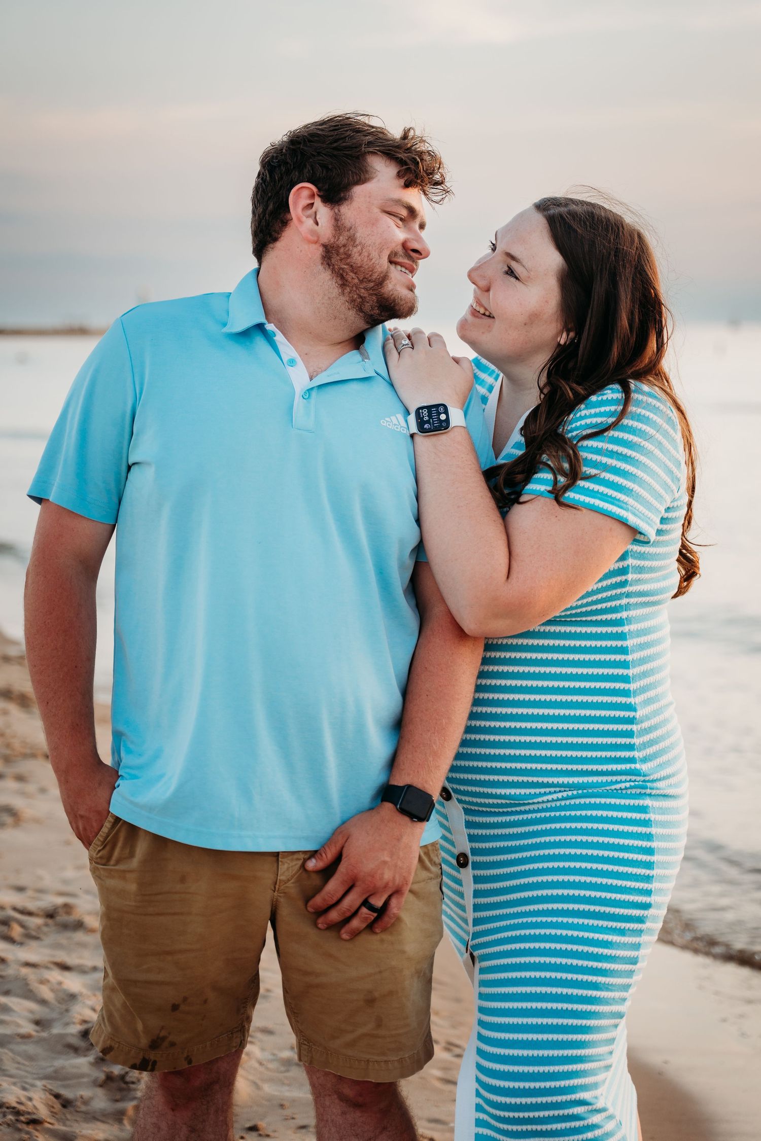 Romantic beachside photo shoot of a couple wearing coordinating turquoise and white outfits at sunset.