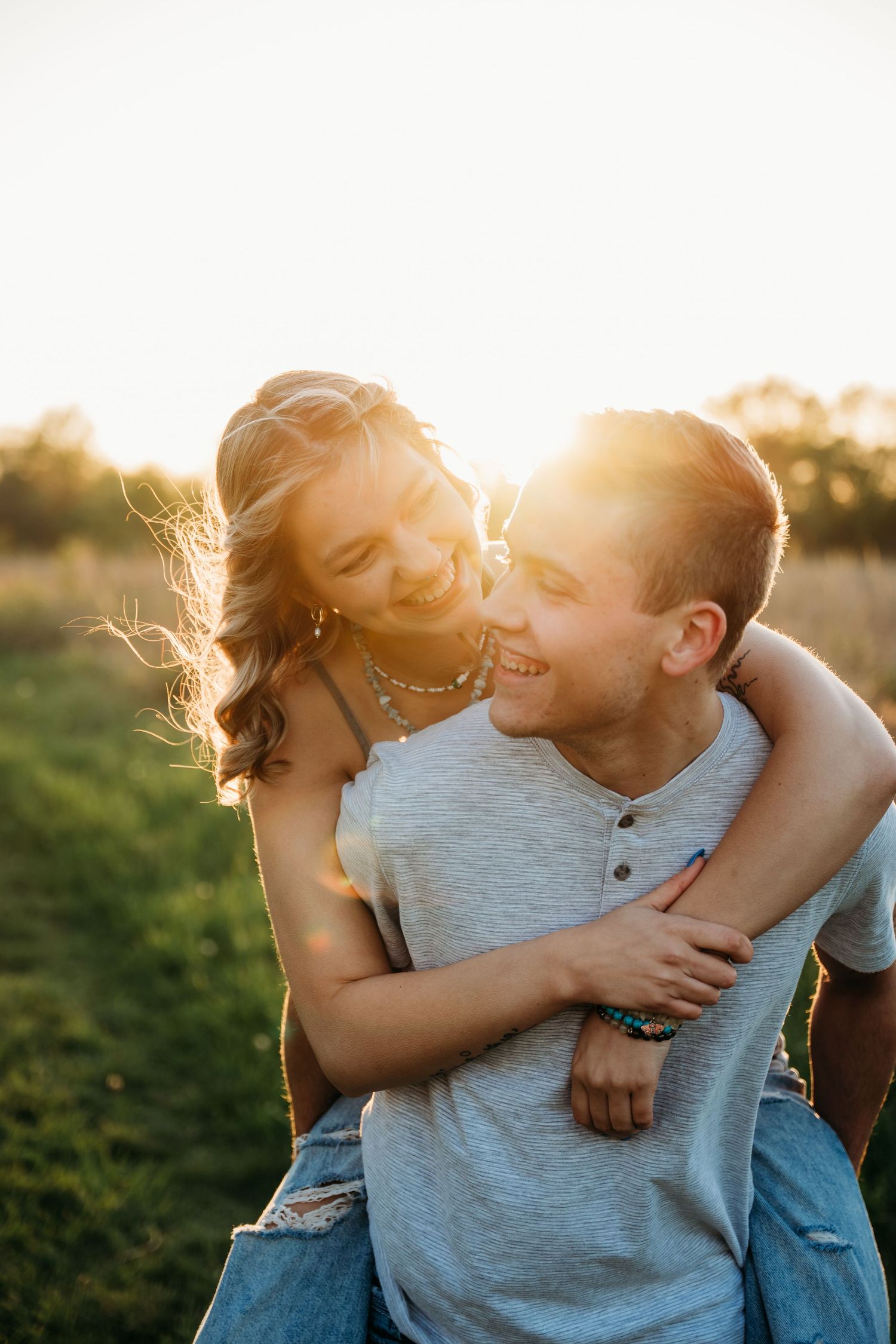 A couple shares an intimate moment backlit by golden sunset light in a summer field.