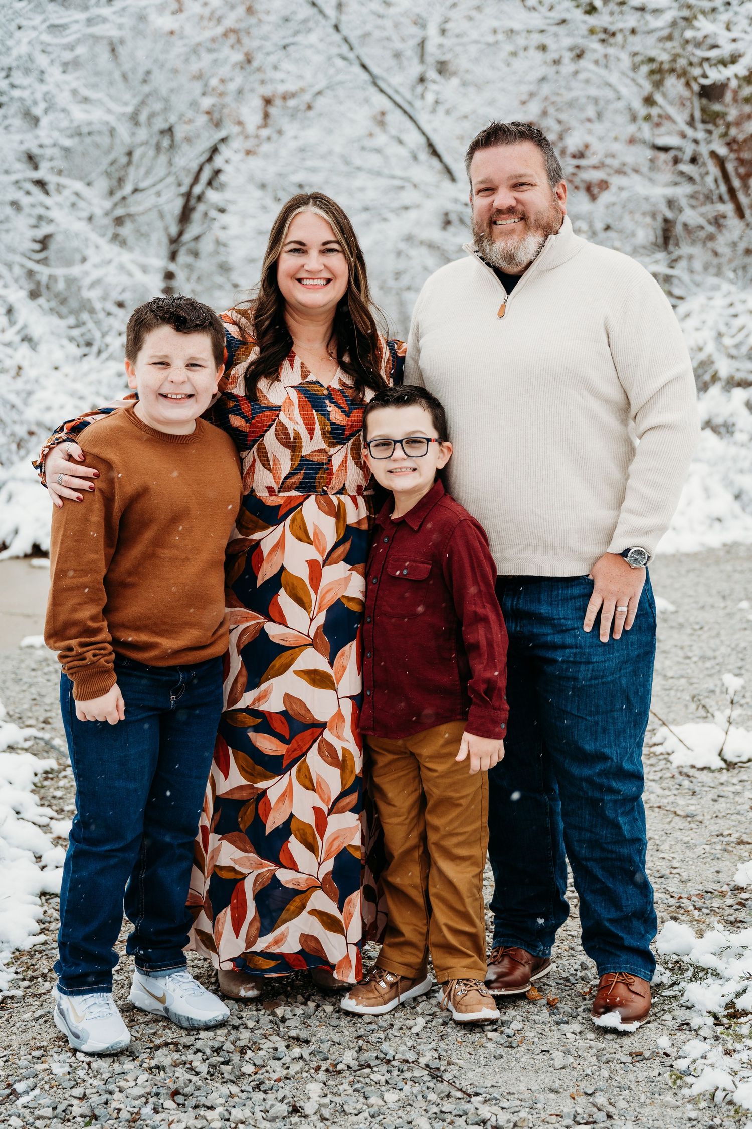A group poses together outdoors in coordinated brown and burgundy outfits against a snowy winter backdrop.