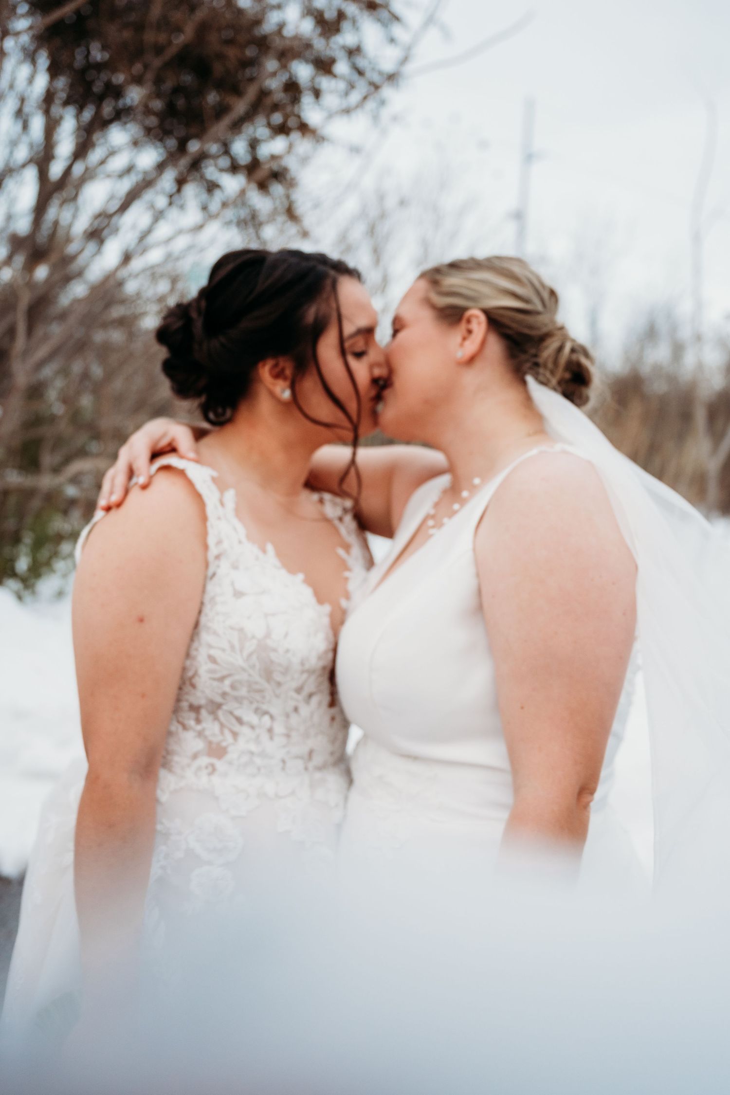 Close-up of two white wedding dresses with delicate lace details in a winter setting.