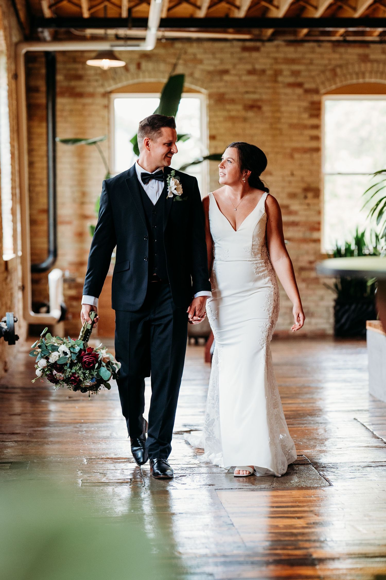 Wedding couple walking together through an elegant brick-walled venue with natural lighting.