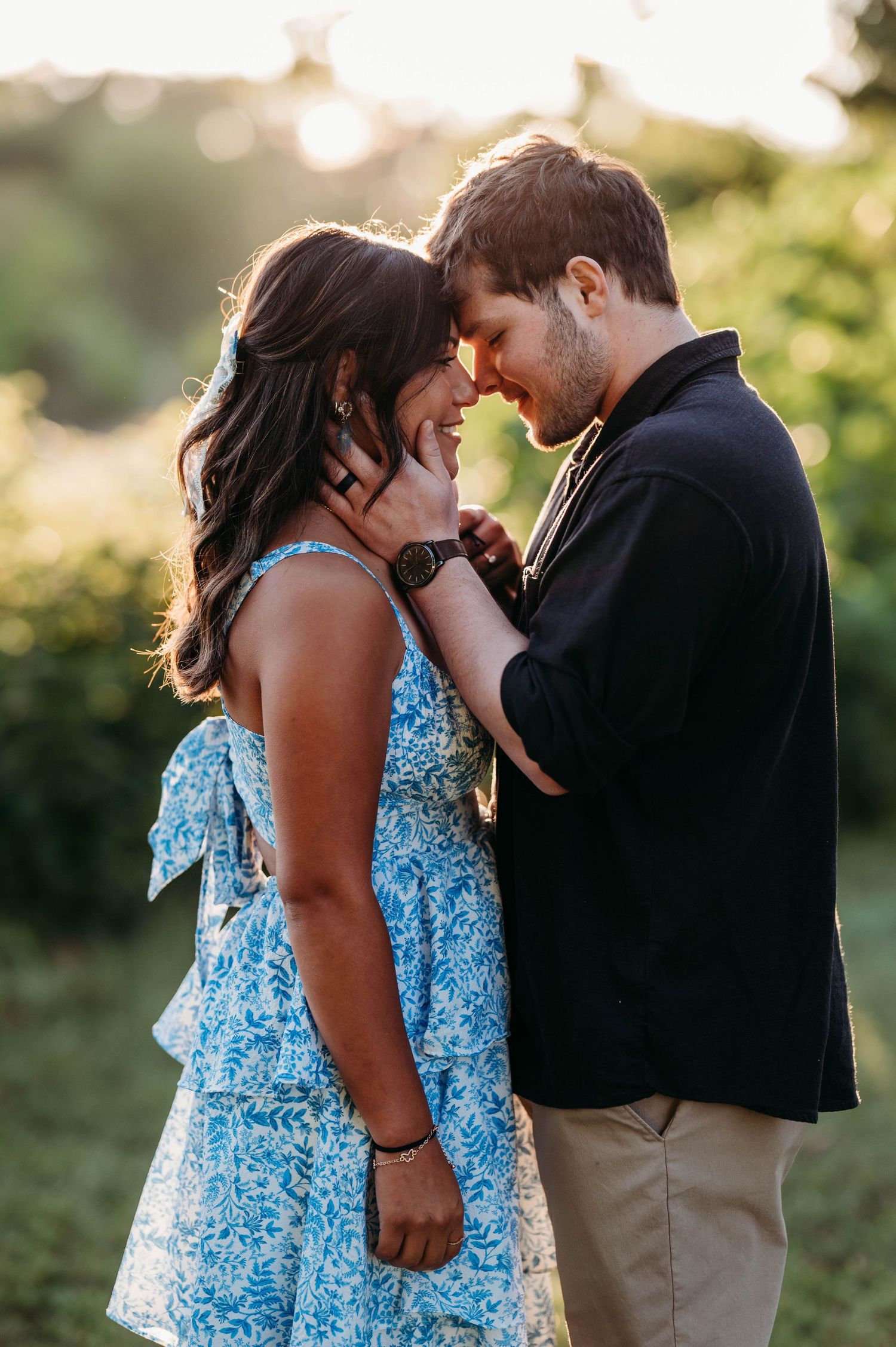 Romantic couple embracing in a natural setting with sunlit background and contrasting black and blue outfits.