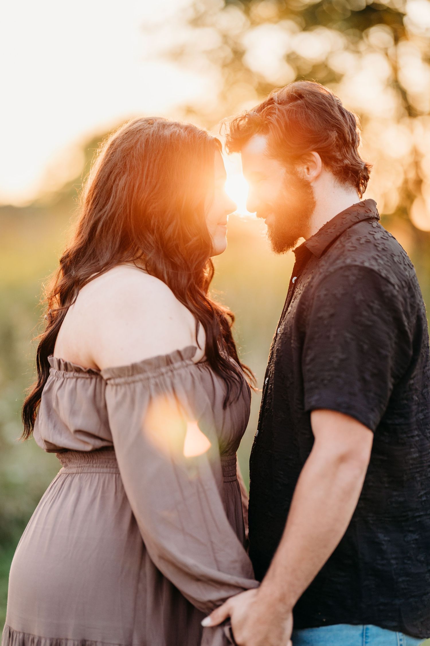 A couple shares a tender moment in warm sunset light, with a soft glow illuminating their silhouettes.