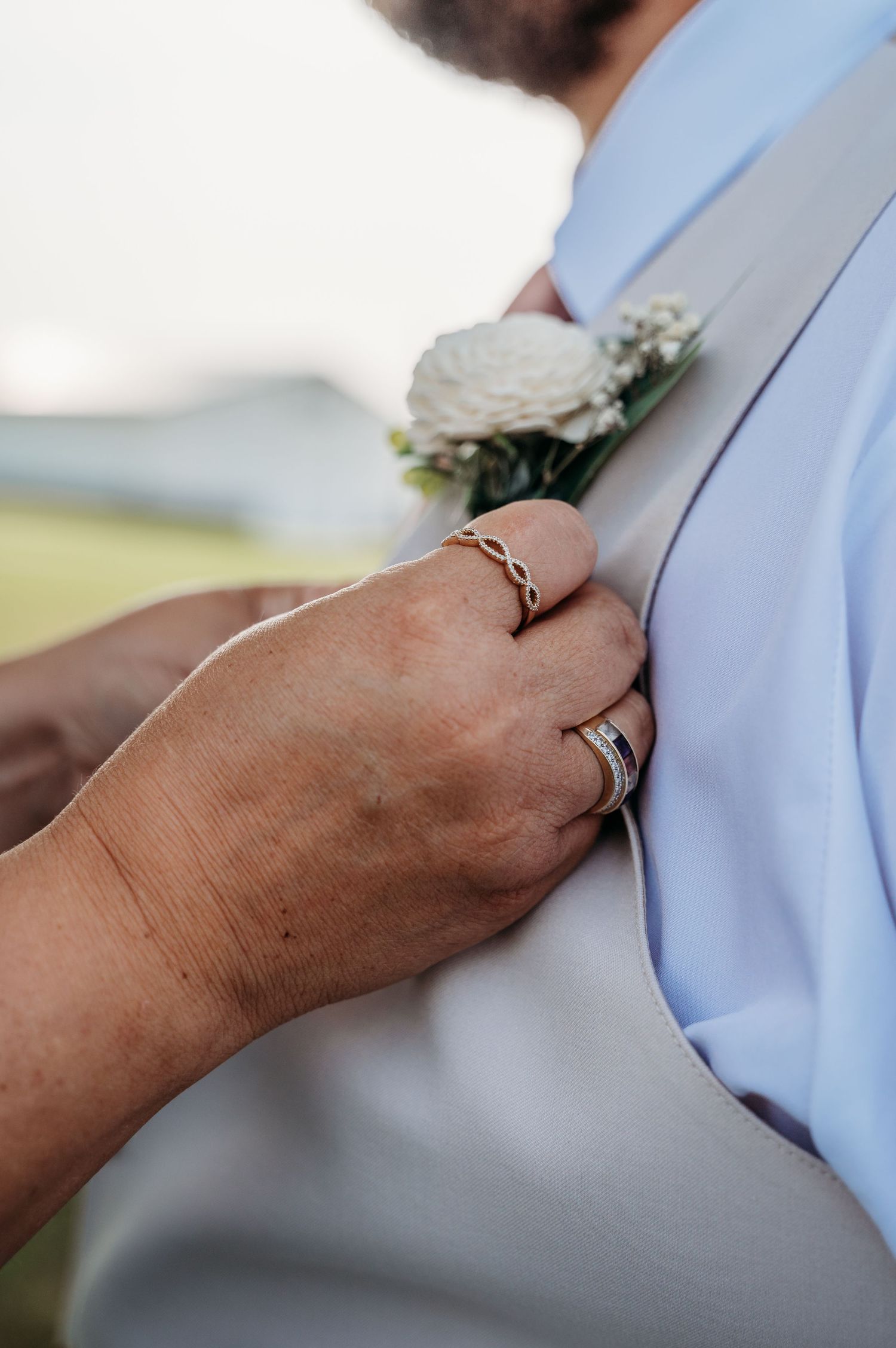 Close-up of hands adjusting a light blue dress shirt and boutonniere during wedding preparations.