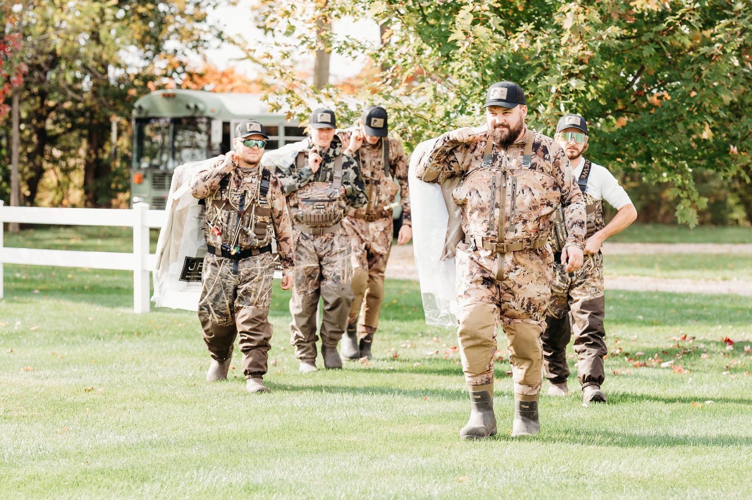 Military personnel in camouflage uniforms march in formation across a grassy field during training exercises.