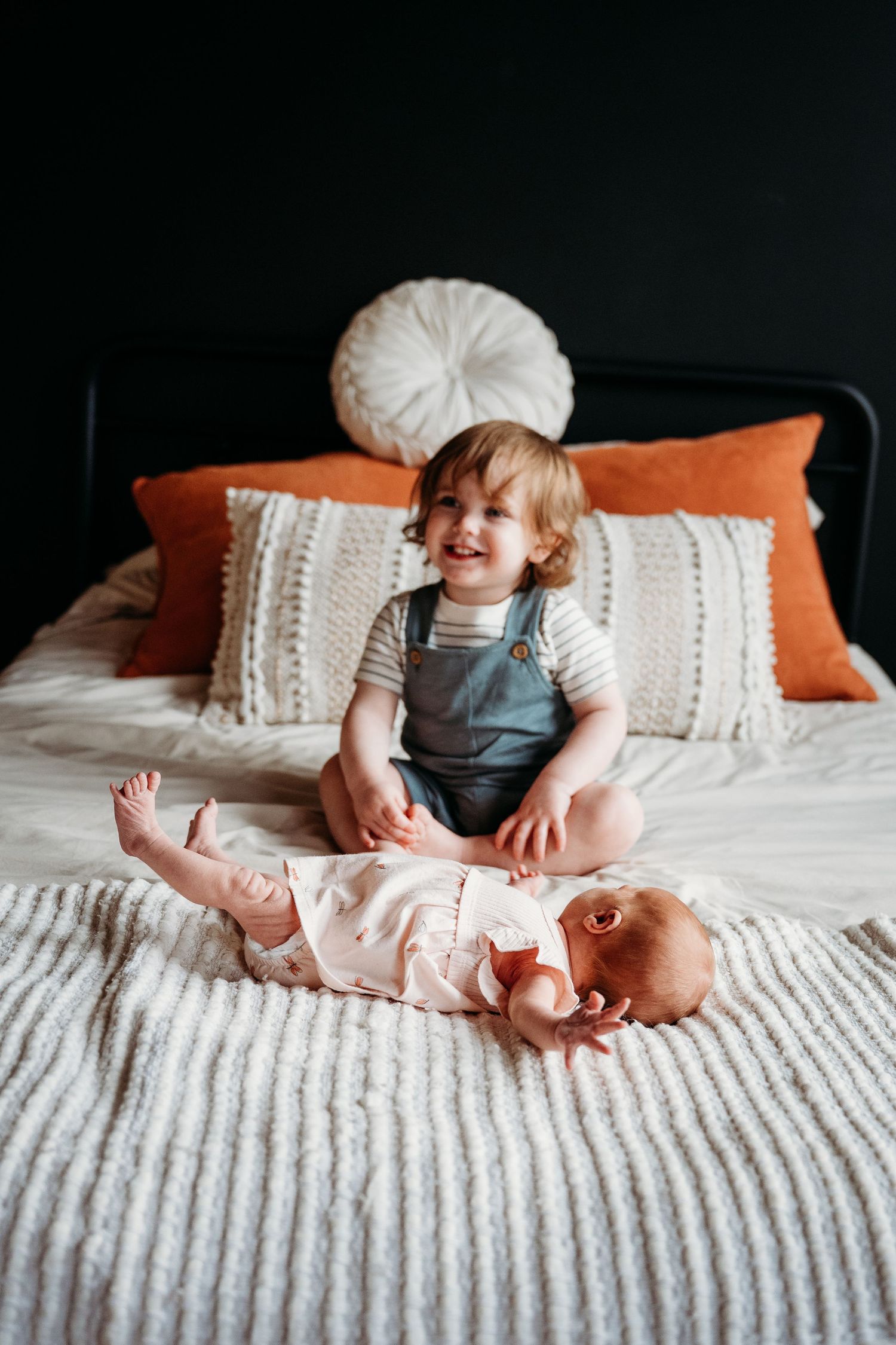 A sequence of photos showing a baby sitting and playing on a white bed with orange accent pillows.