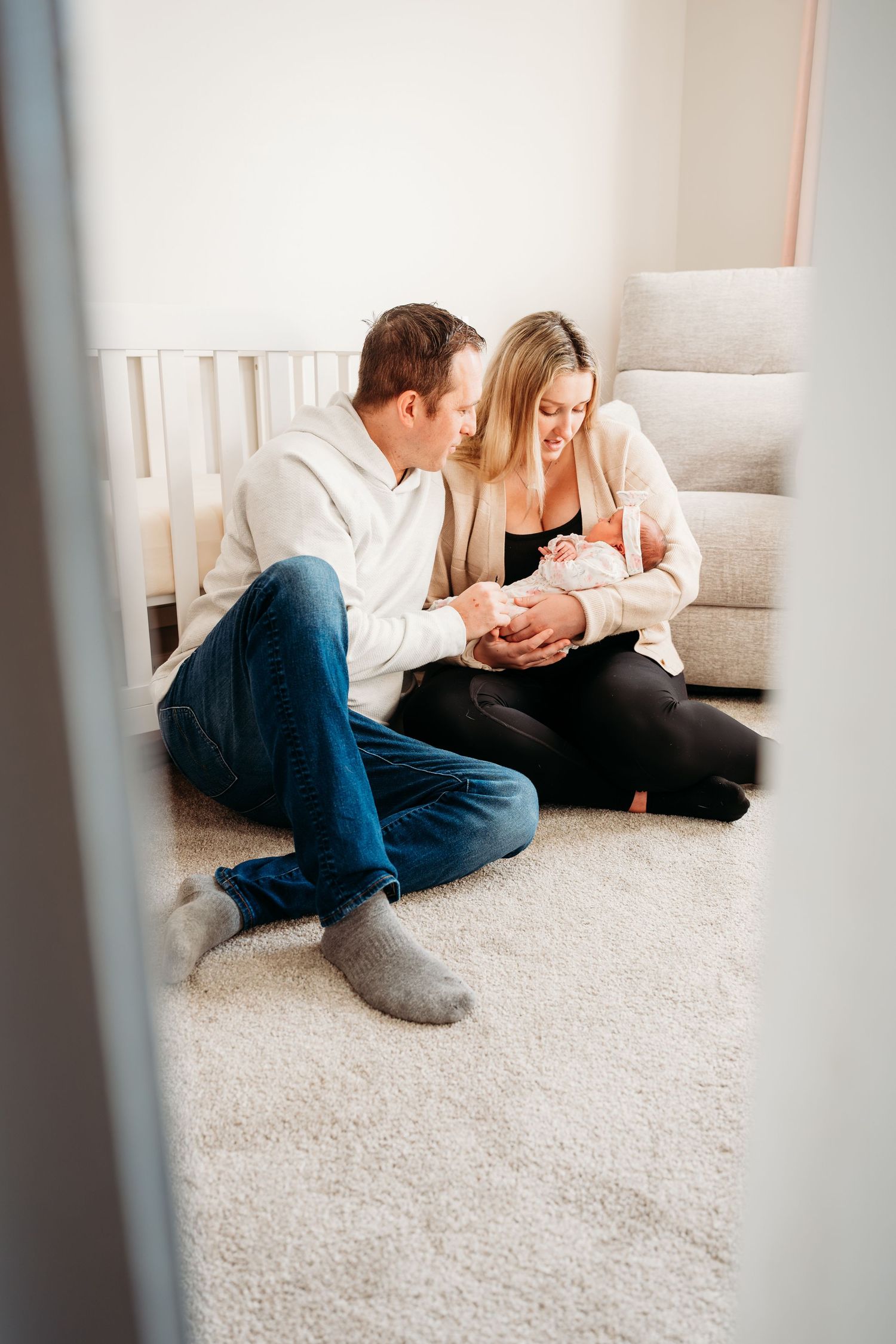 A couple lies together on a white carpet, sharing an intimate moment in a bright, minimalist interior setting.