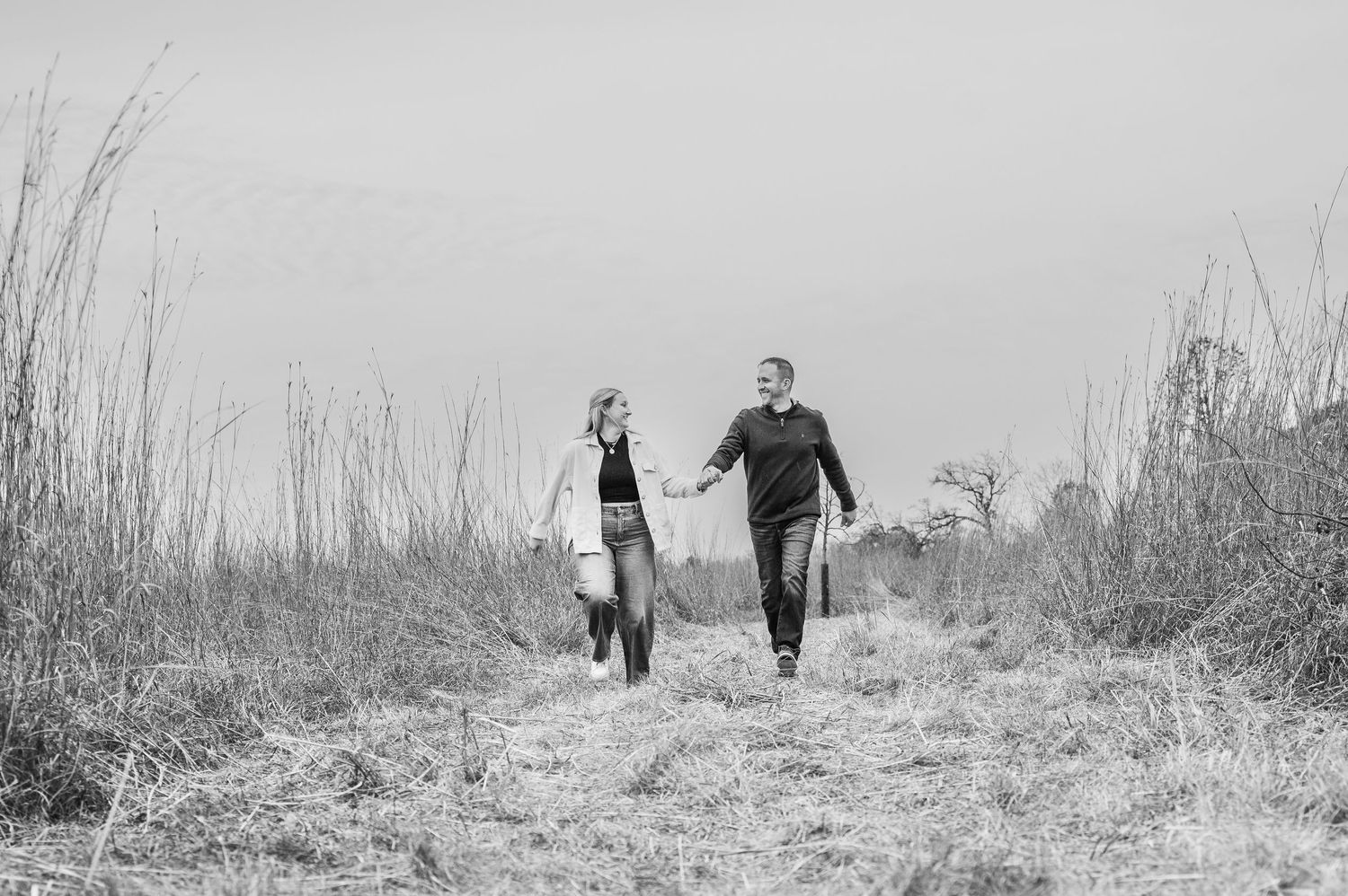 Black and white photo of couple walking hand in hand along a nature path.