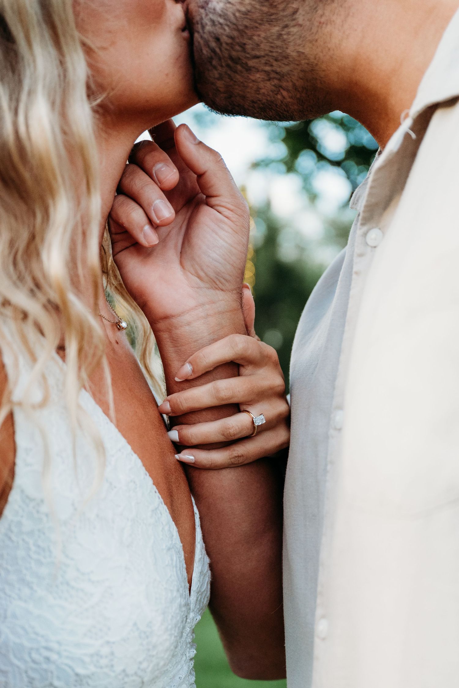 Close-up of couple holding hands at wedding with bride in lace dress and soft bokeh background.