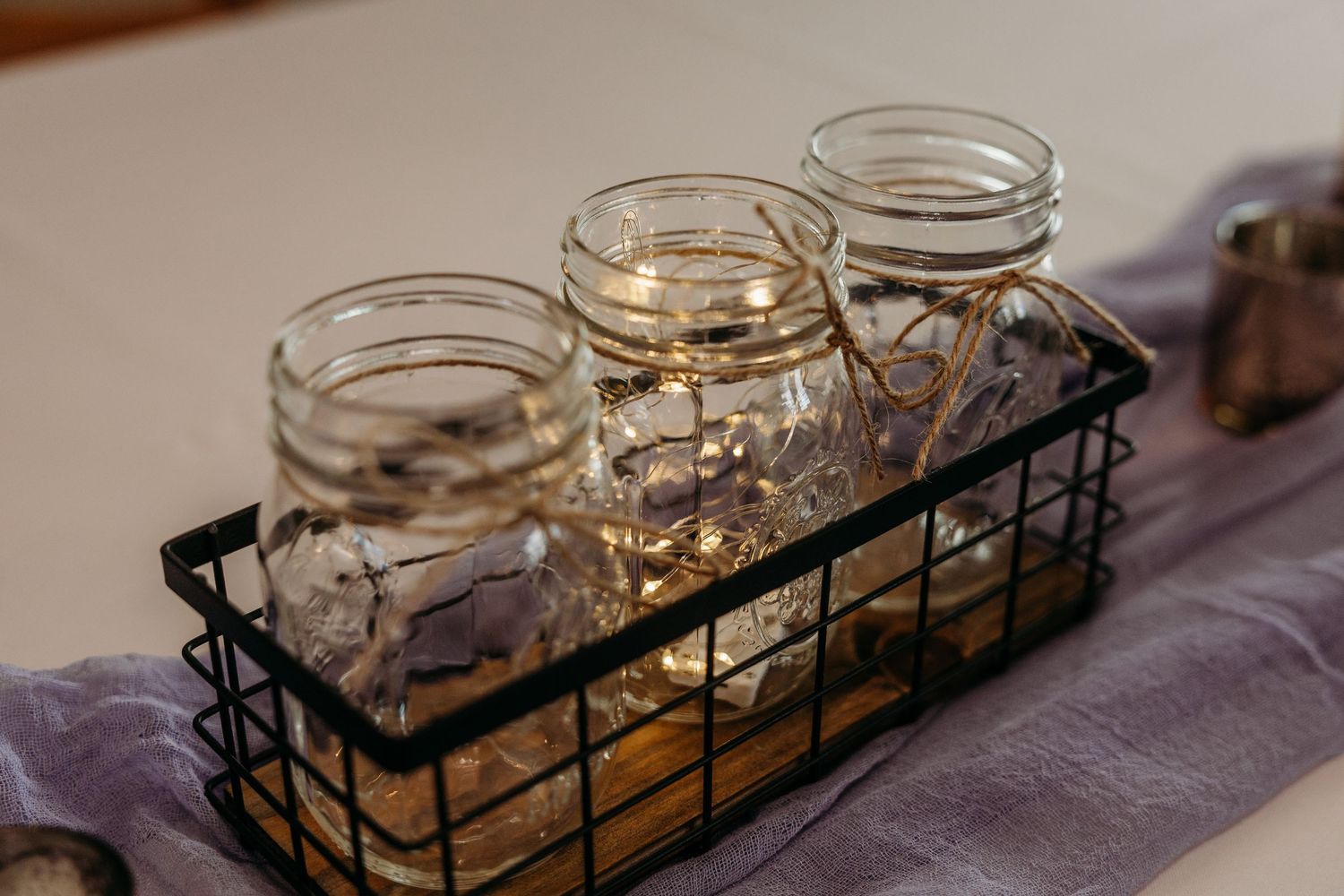 A series of glass mason jars arranged in a black metal holder on a gray tablecloth.