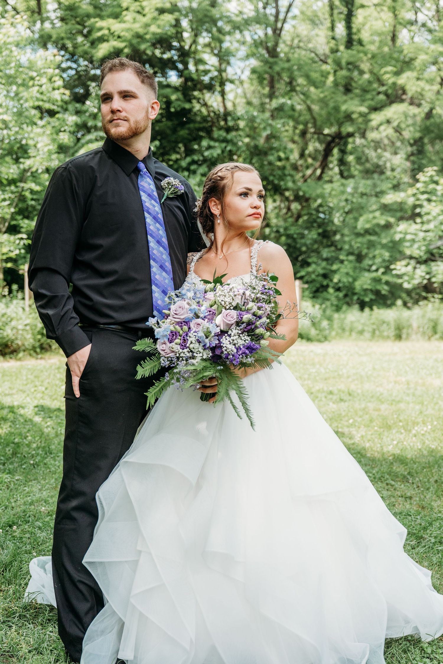 A bride in a flowing white ballgown and groom in black suit walk together through a lush garden setting.