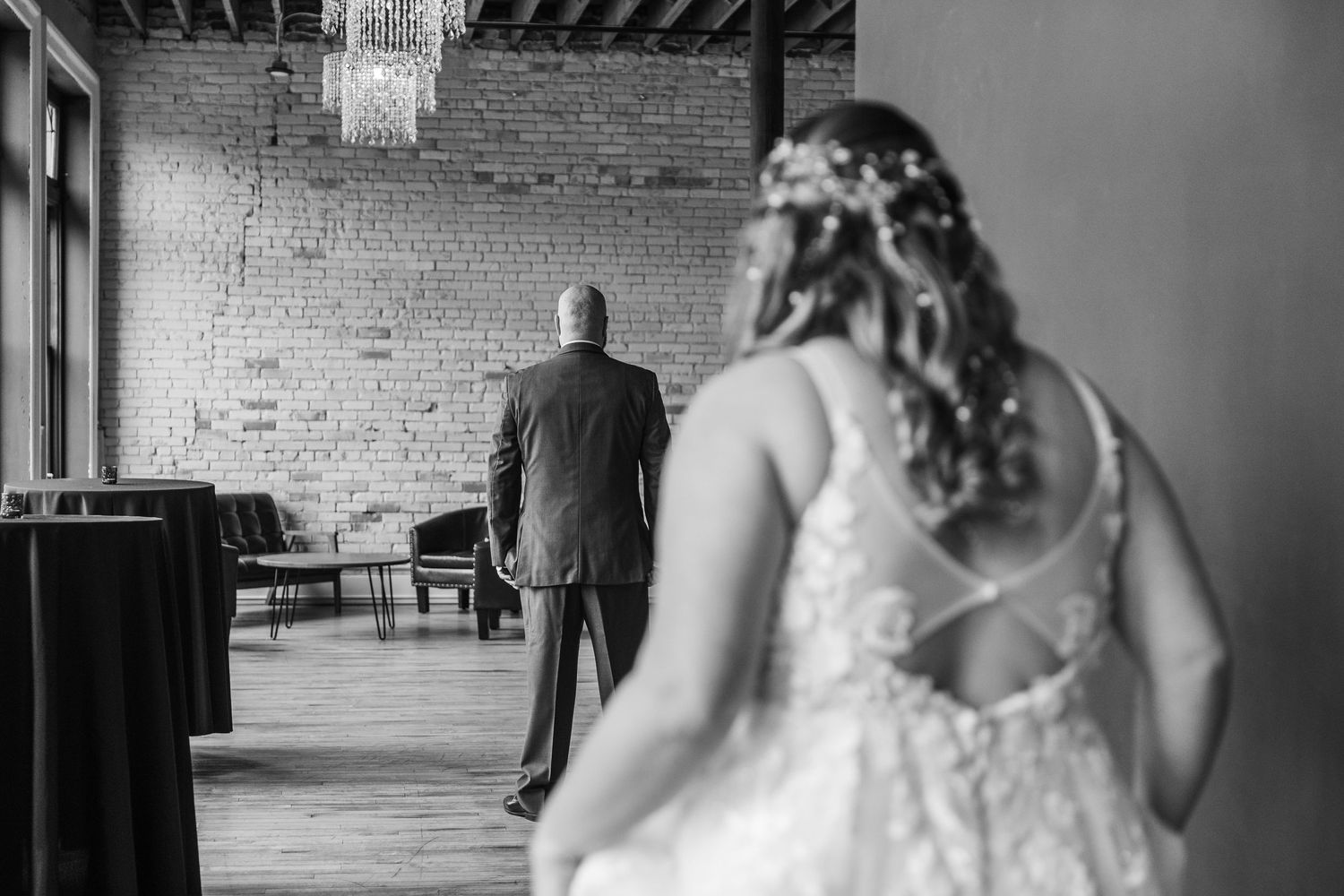 A black and white wedding photo capturing a dramatic moment between two figures in an industrial brick venue.