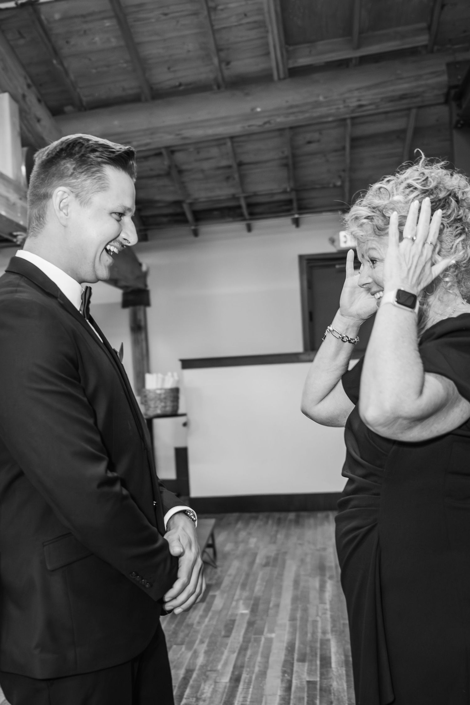 A couple in formal attire share a playful moment together while covering their faces in a spacious indoor venue.