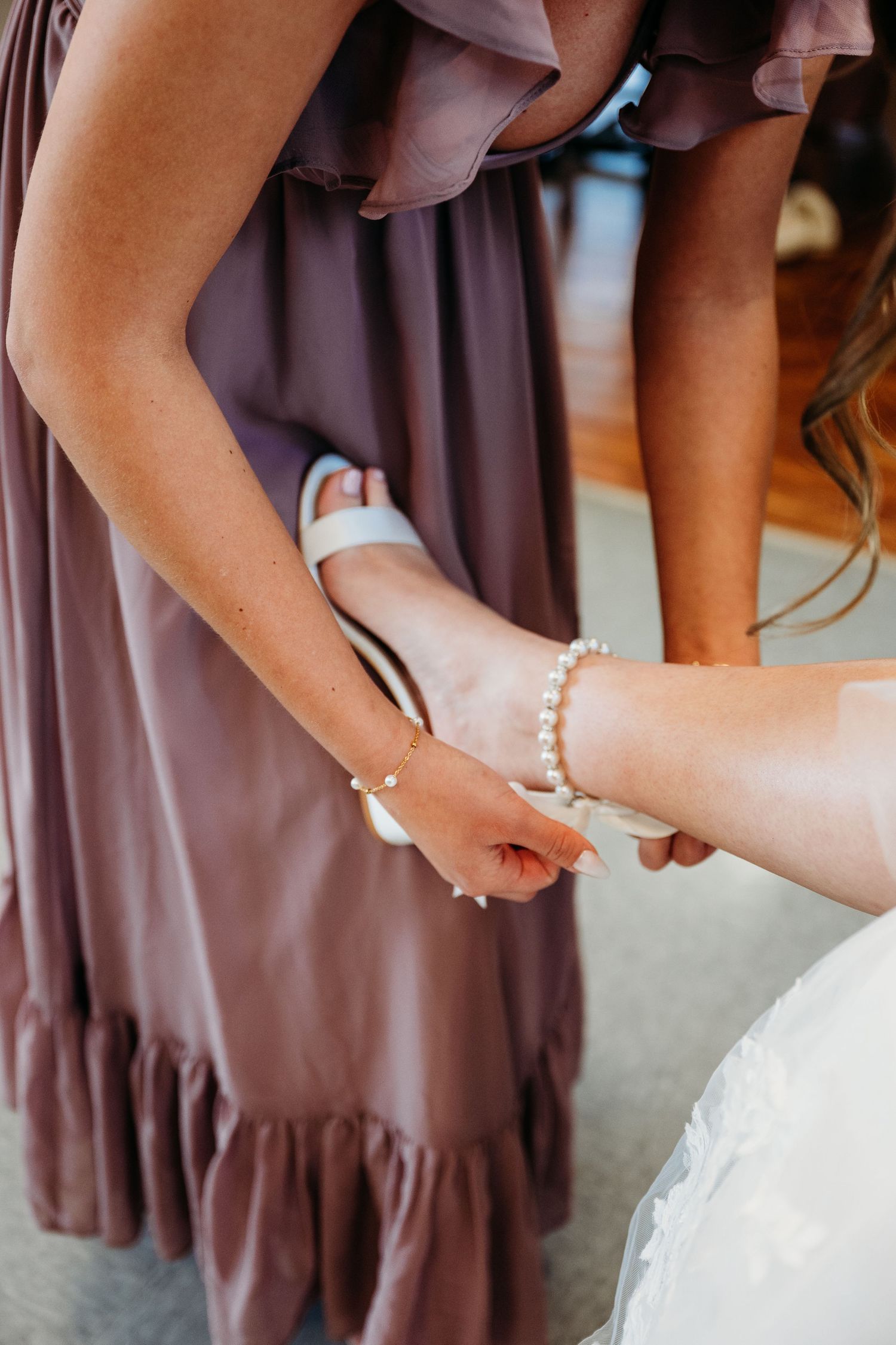 Four bridesmaids in brown dresses help adjust the bride's white wedding gown in elegant preparation scene.