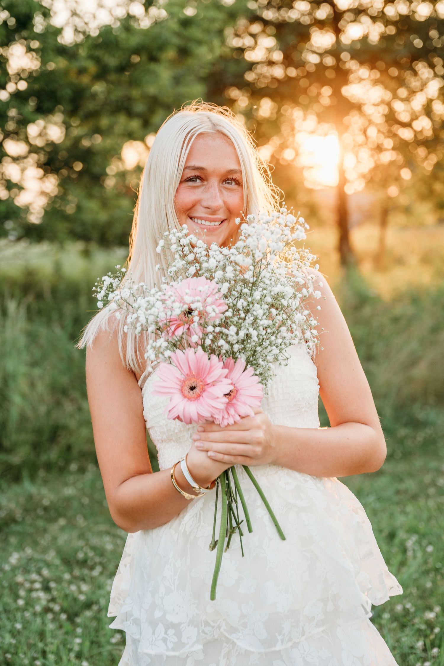 Delicate pink gerbera daisies and baby's breath bouquet held in summer sunlight.