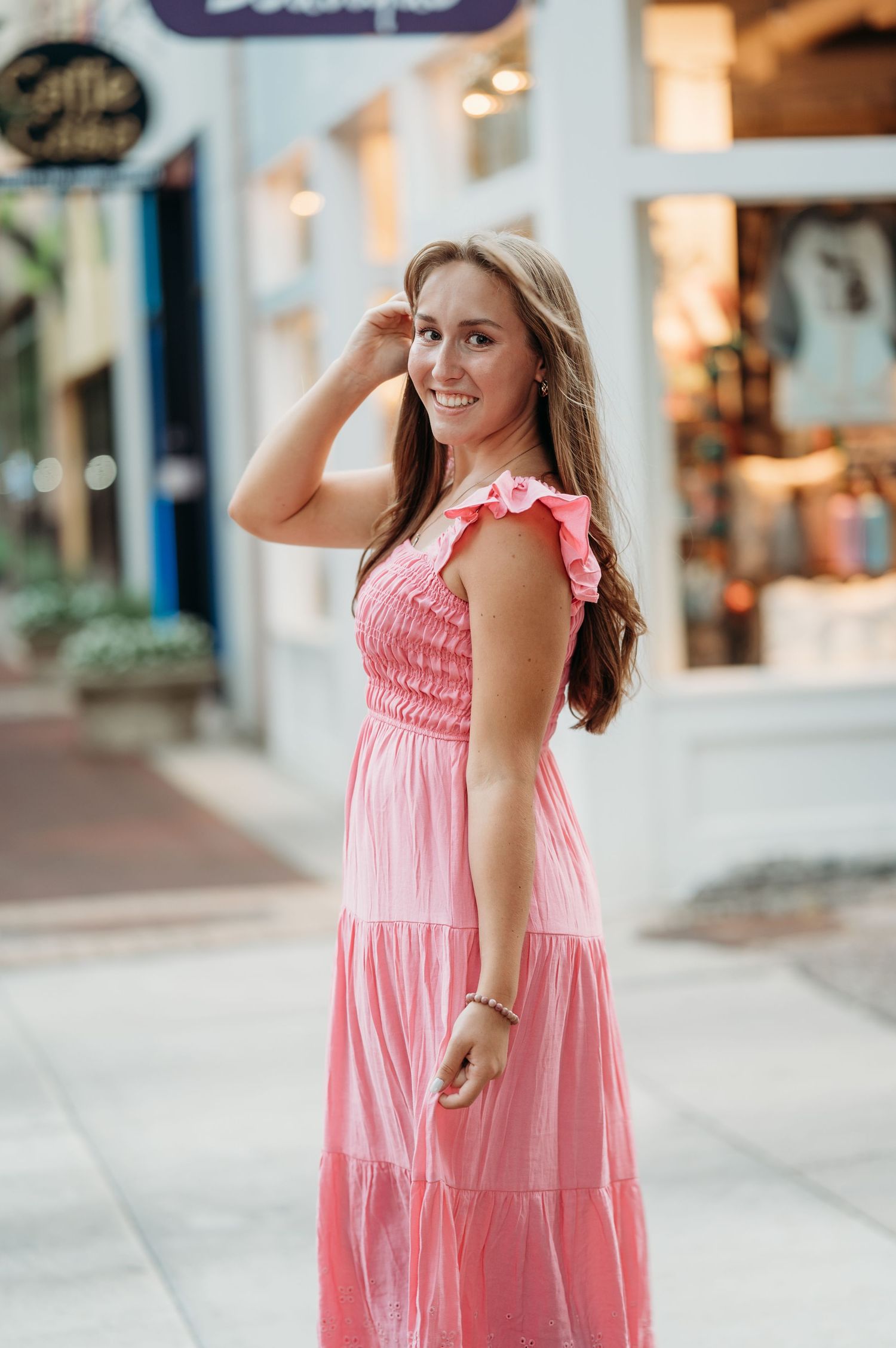 A person wearing a pink ruffle-sleeved maxi dress poses on a city street with storefronts in the background.
