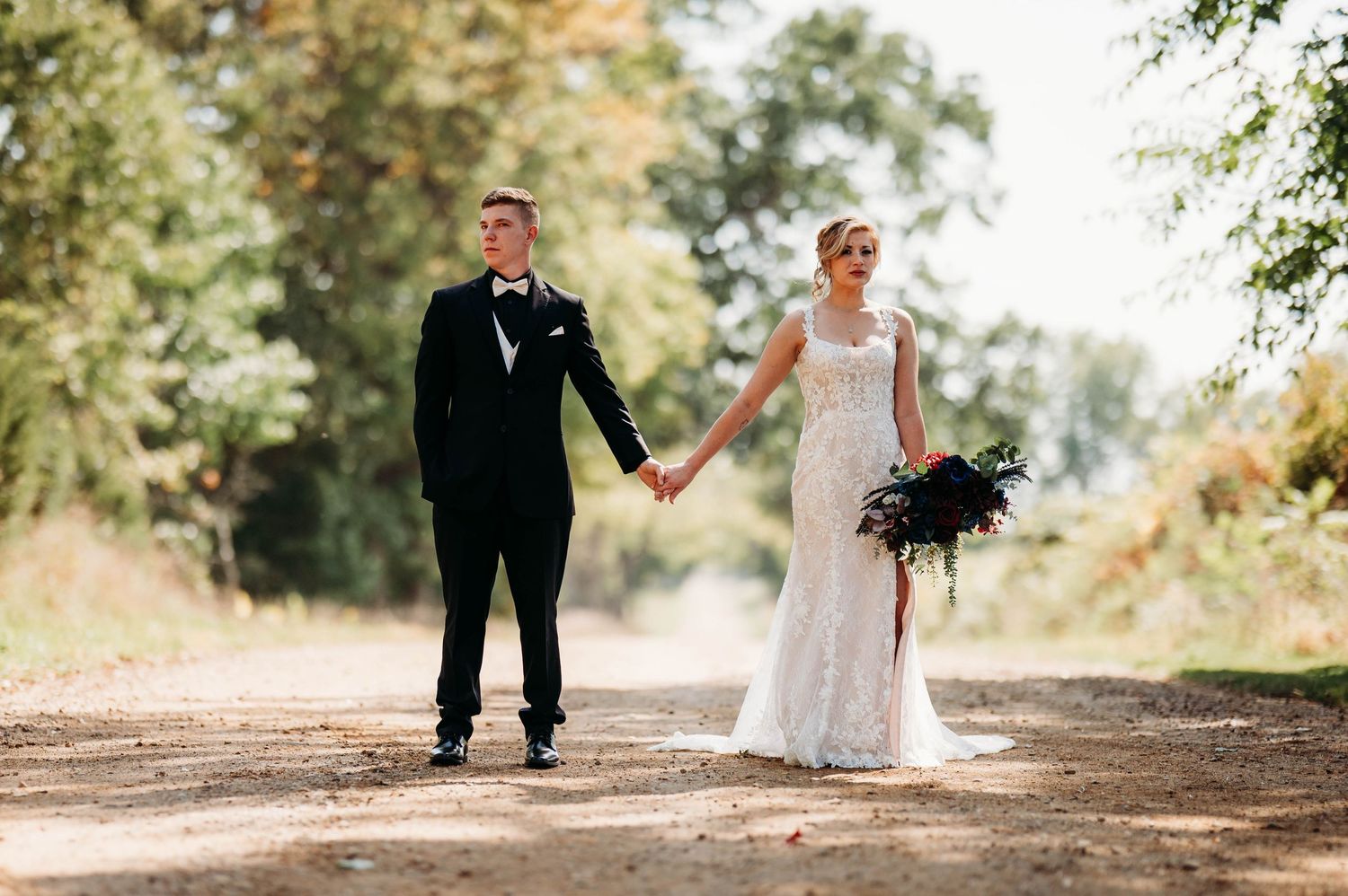 A romantic wedding couple walks hand in hand down a tree-lined path during an autumn outdoor photo session.
