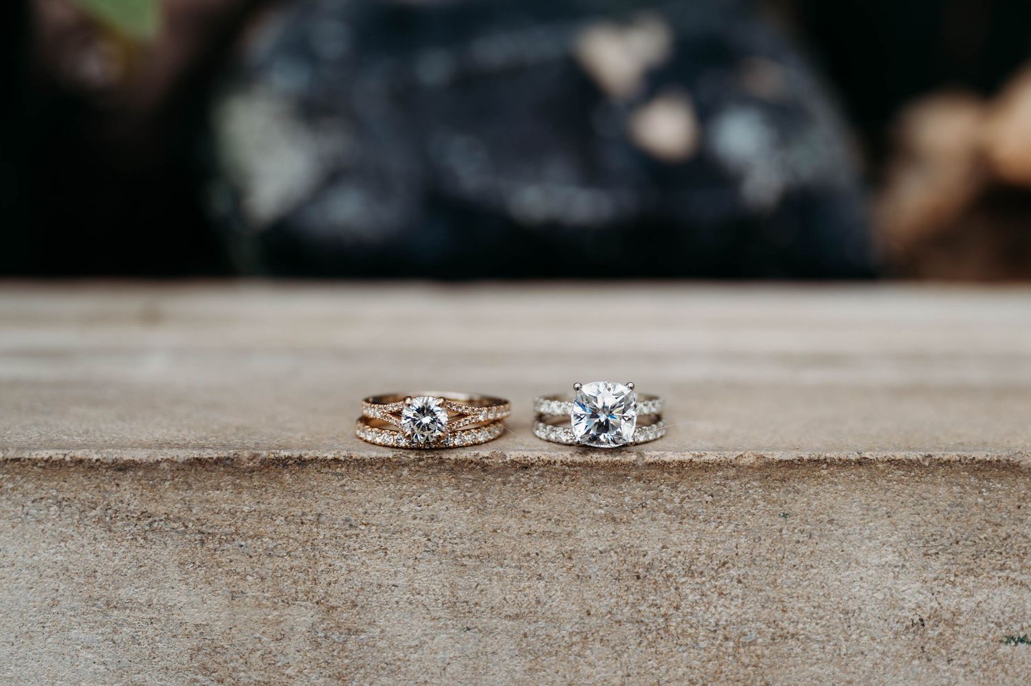Two elegant engagement rings with diamonds sit side by side on a weathered gray concrete surface.