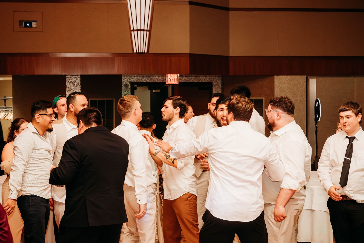 A panoramic view of people dancing and celebrating at an indoor reception with warm lighting and formal attire.