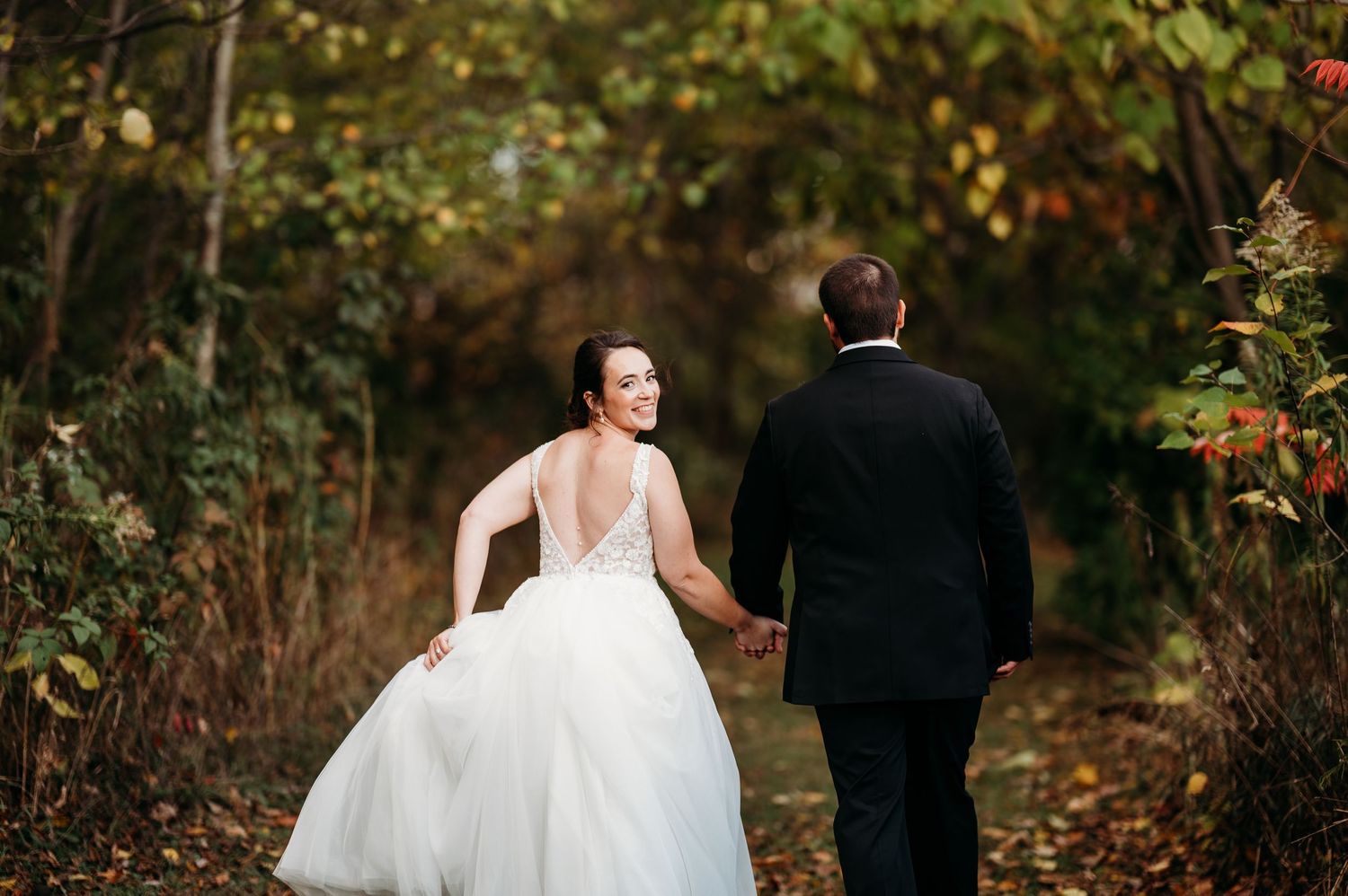 Romantic wedding couple walks through a vibrant autumn forest path with golden foliage.