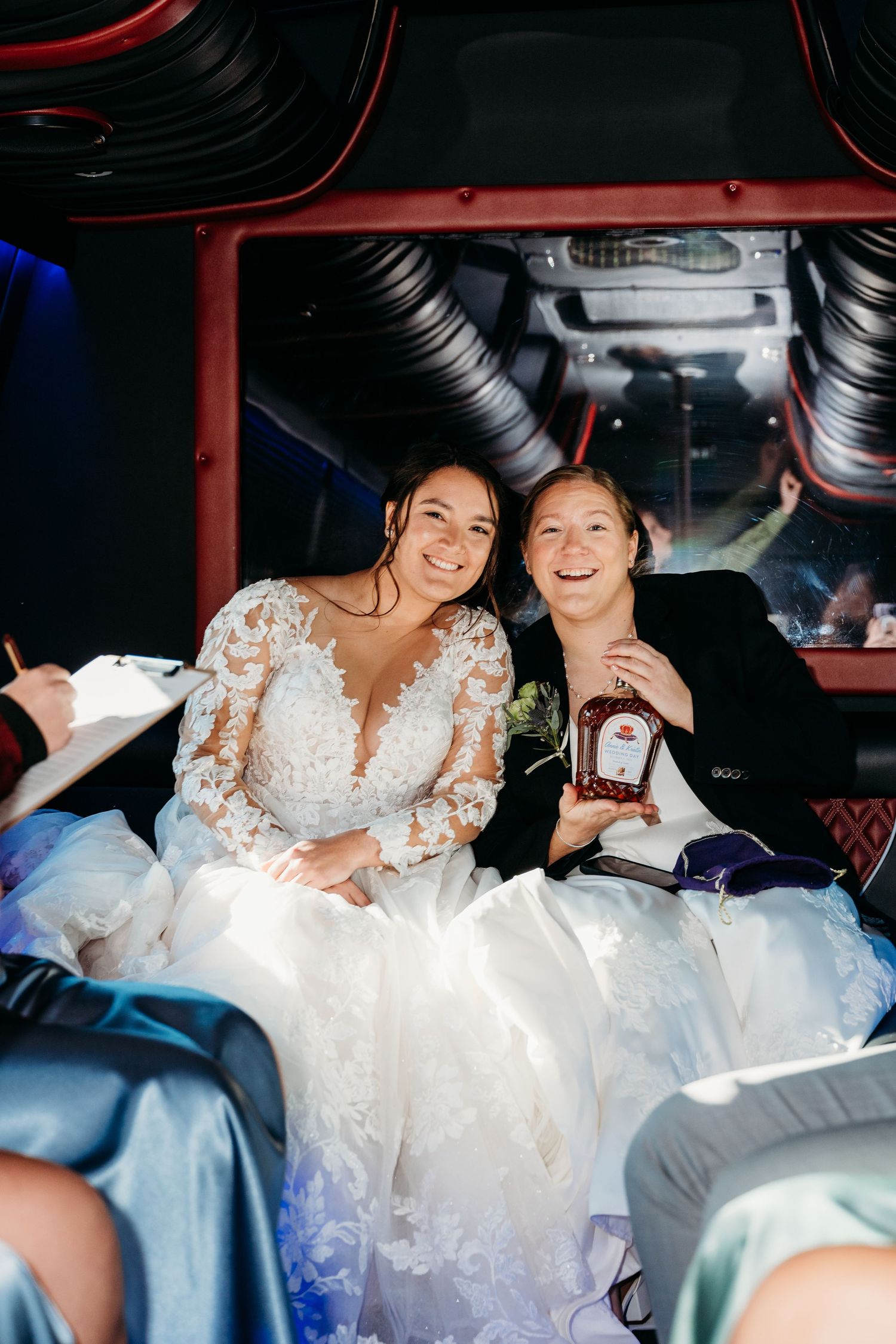Two brides in white wedding dresses share a joyful moment together in the back of a car.