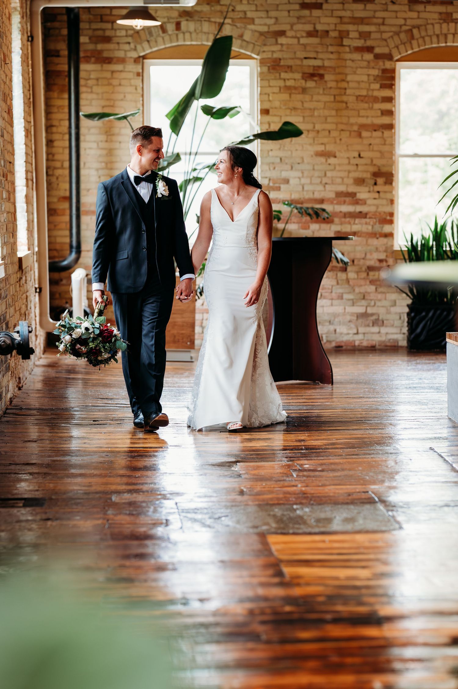 A couple in formal attire dancing together on a polished hardwood floor in a rustic brick-walled venue.