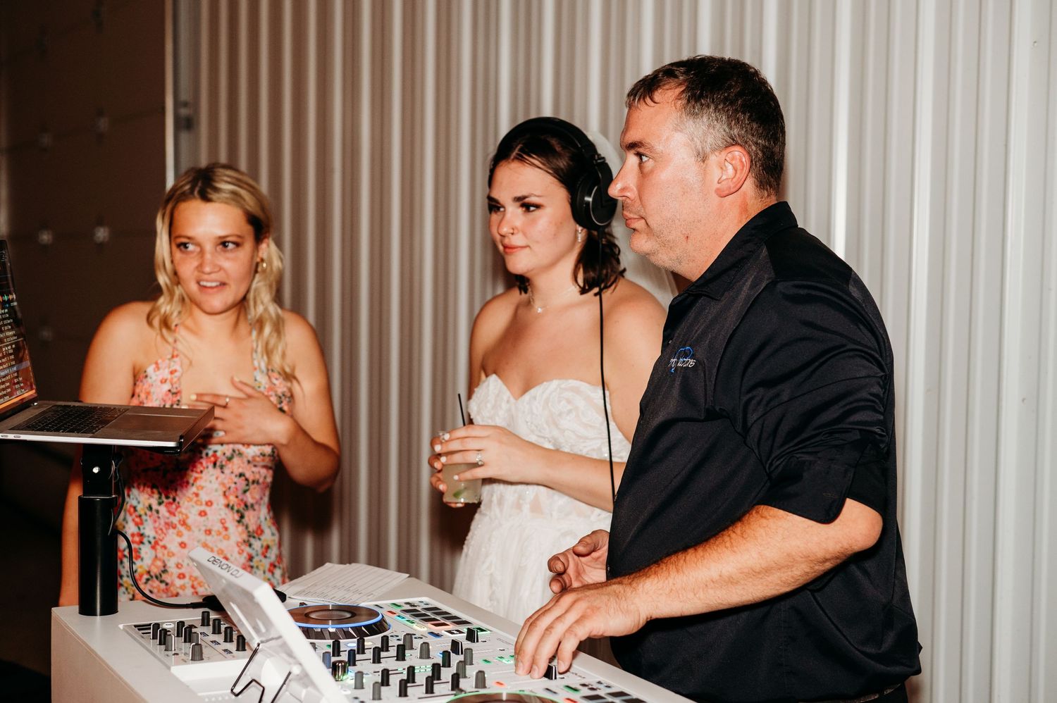 People gathered around DJ equipment at an event space enjoying a wedding reception party.
