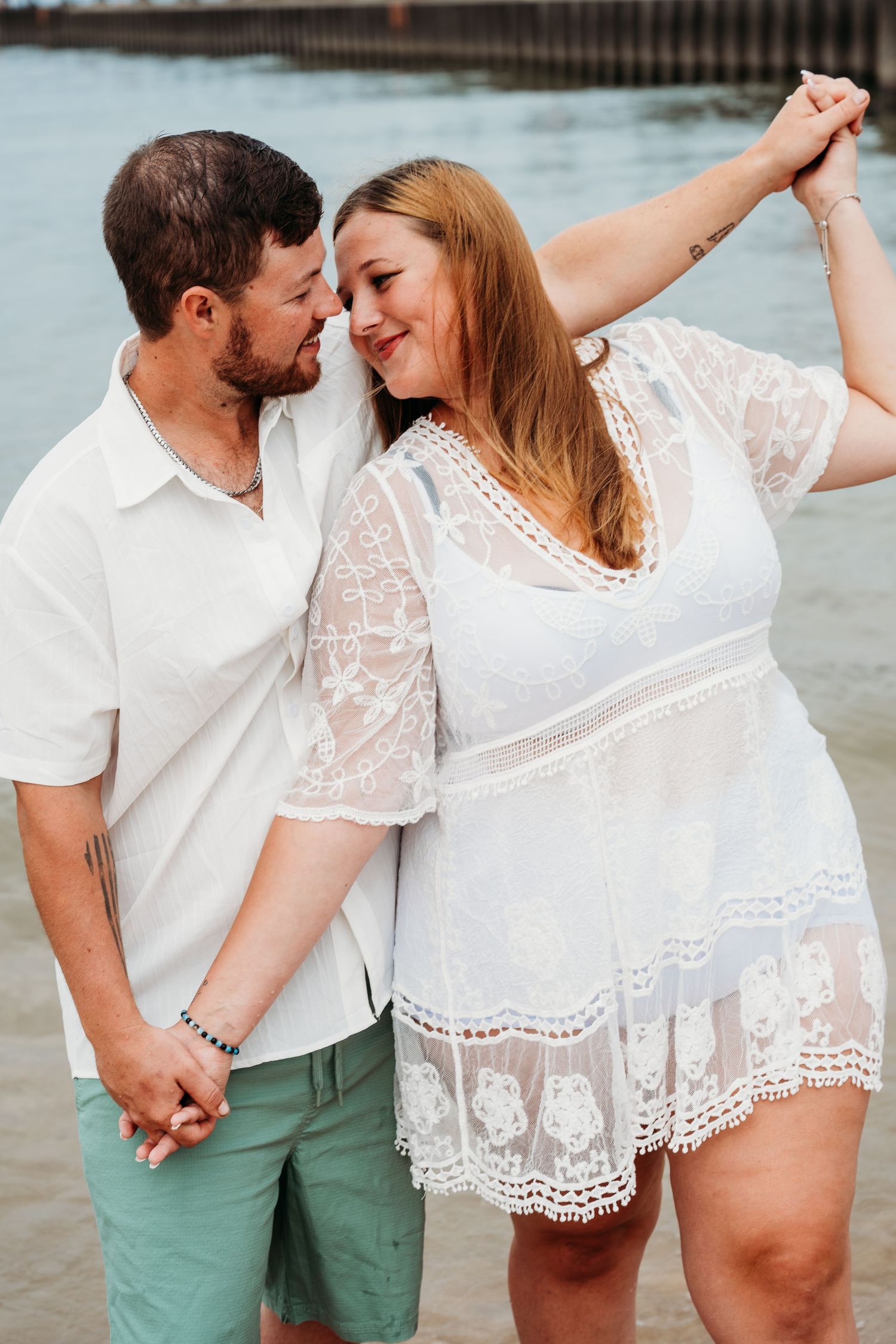 A romantic couple in white and green outfits embracing on the beach in a series of loving poses.
