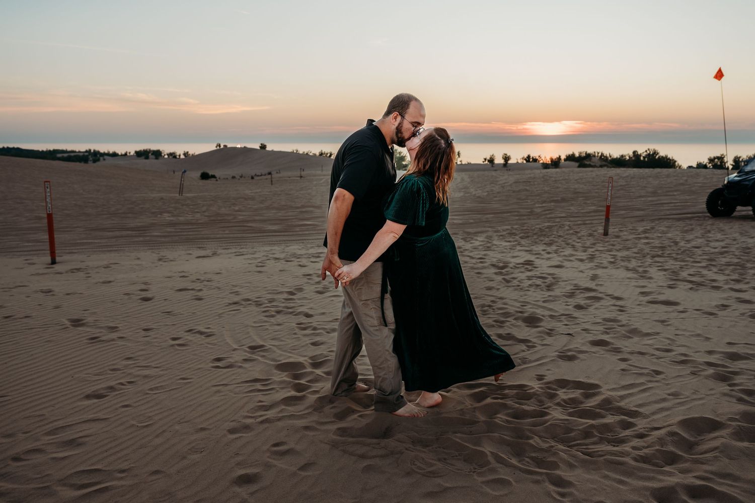 Couple embraces on sandy beach during golden sunset creating romantic silhouettes along the shoreline.