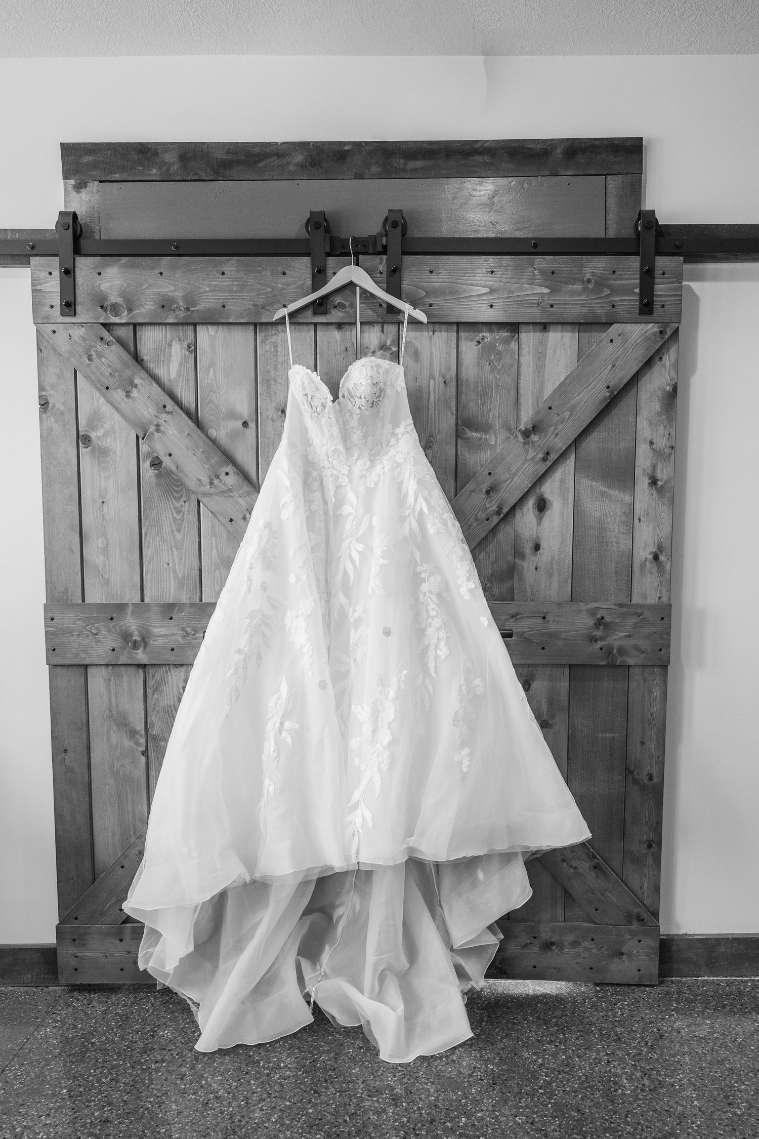 A white wedding dress train displayed against a rustic wooden barn door in a series of black and white photographs.