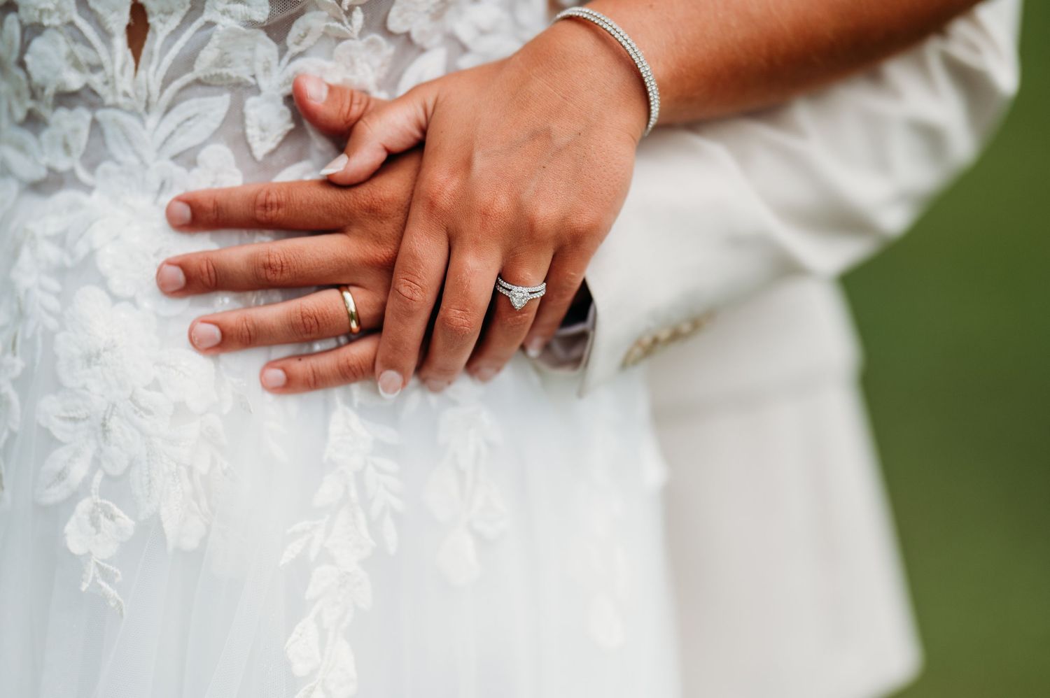 Close-up view of hands touching white lace wedding dress fabric against a green background.