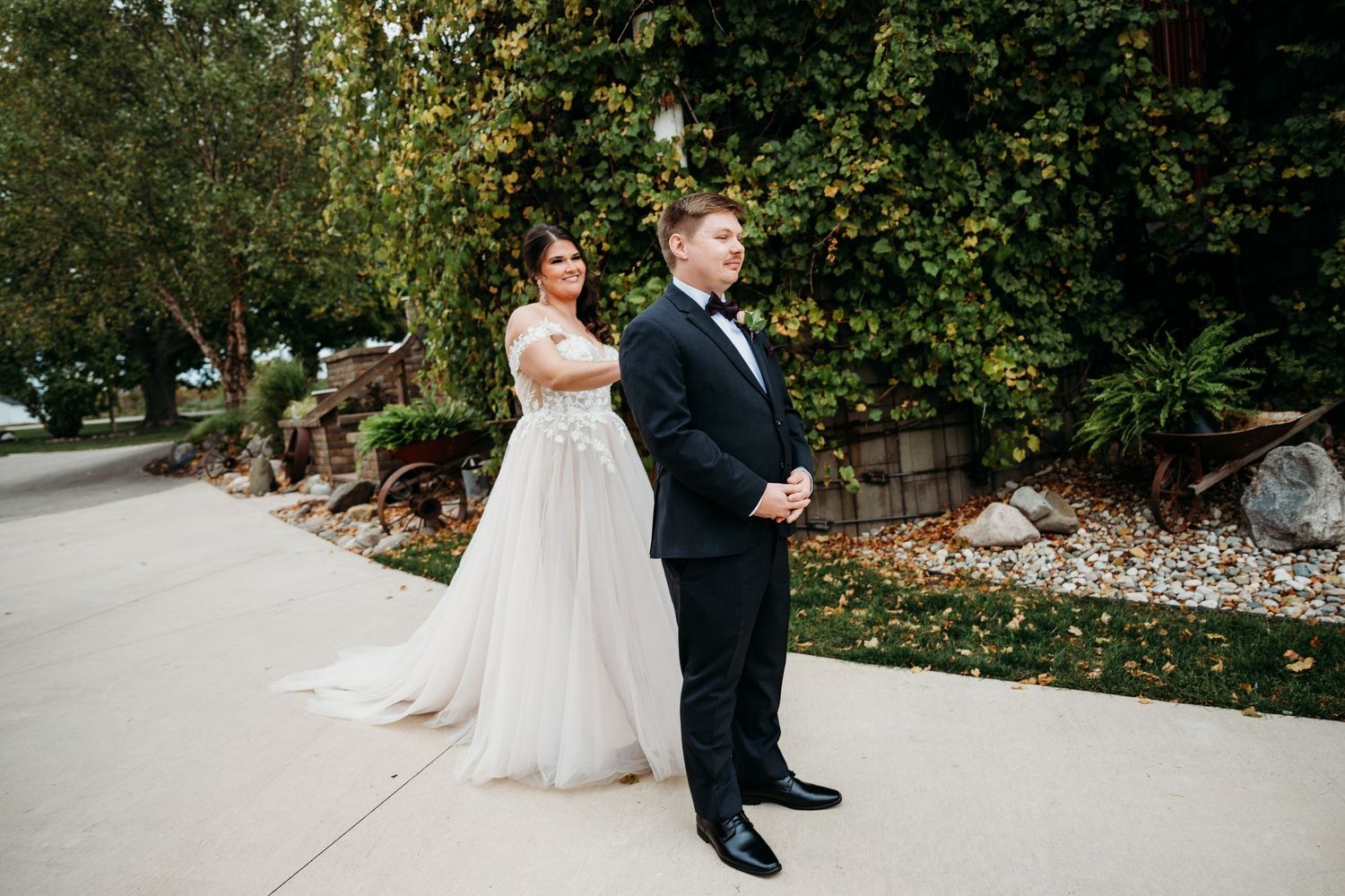 Wedding couple poses together on landscaped garden path surrounded by lush greenery.