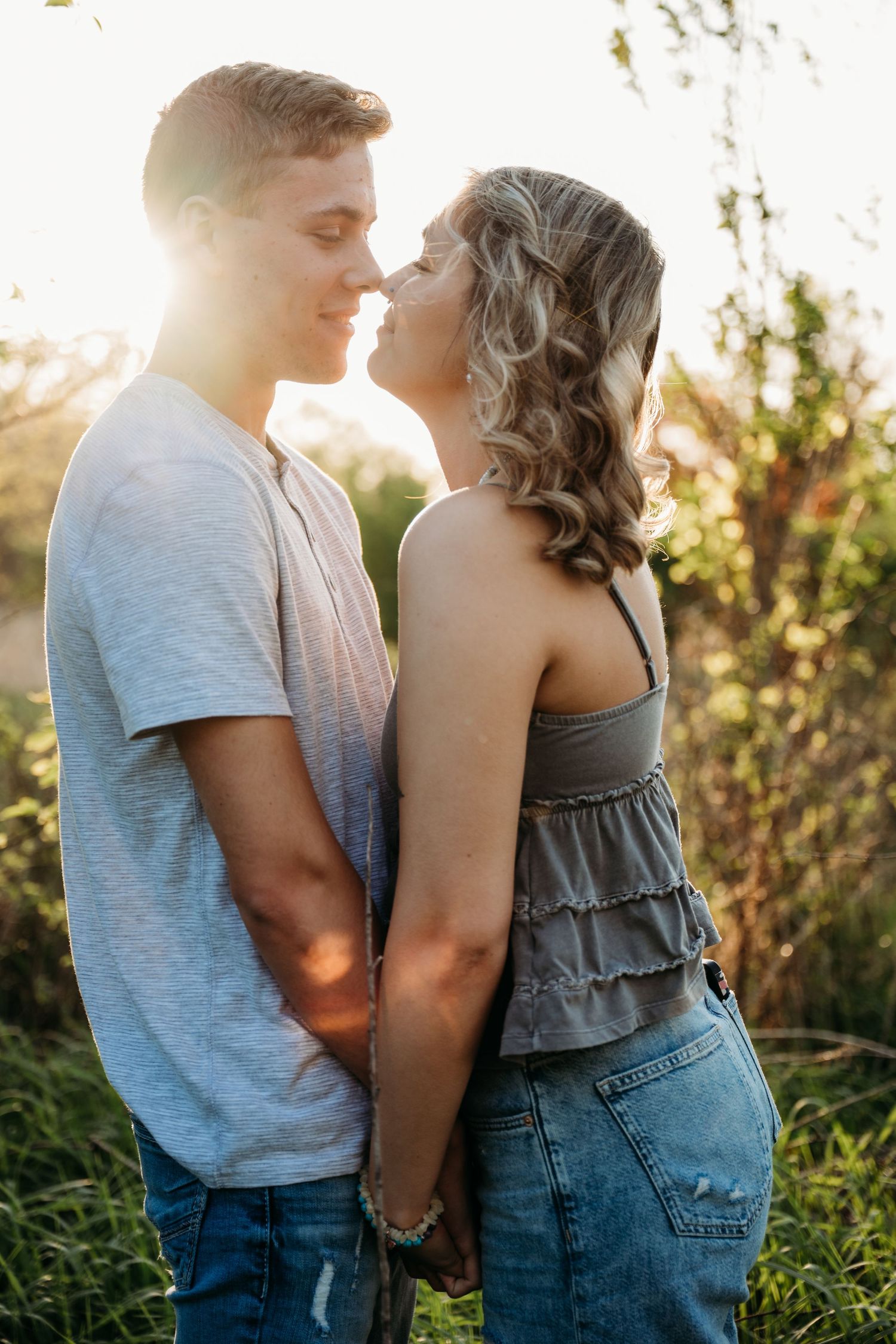 A romantic couple shares an intimate moment at sunset in a field with golden light streaming through the foliage.