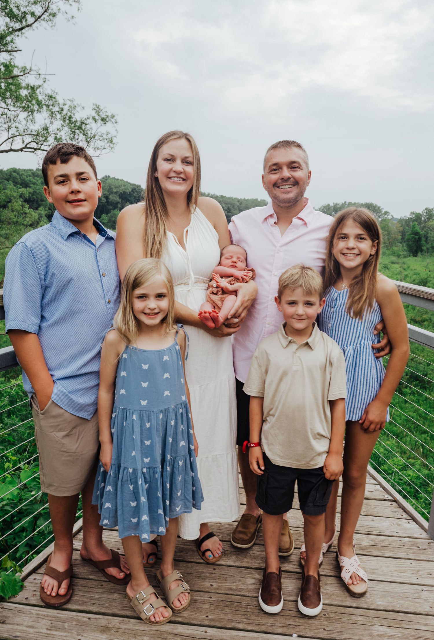 Family poses together outdoors on wooden deck with lush green mountains in background.