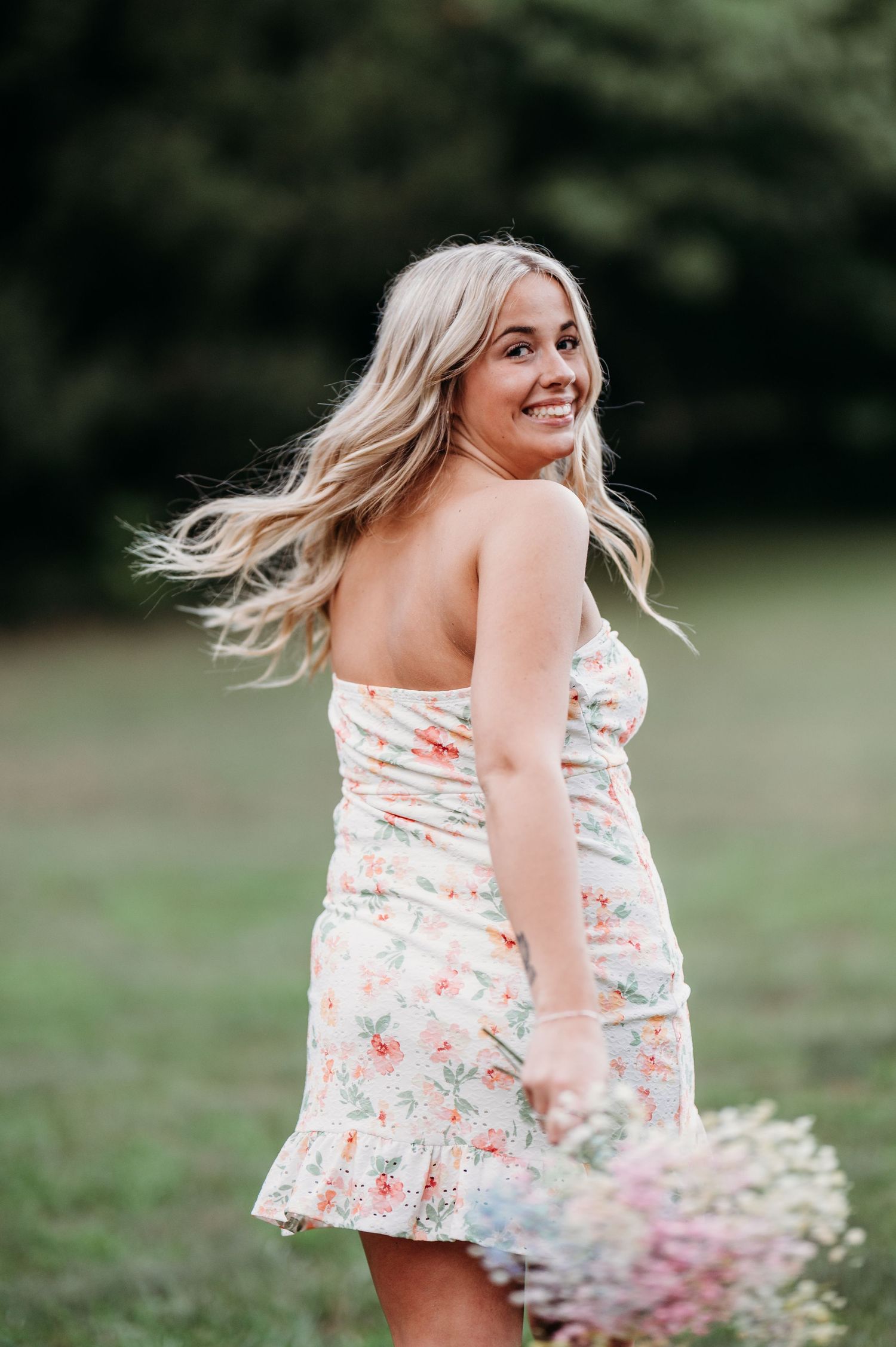 A person in a floral sundress twirls joyfully in a grassy field on a summer day.