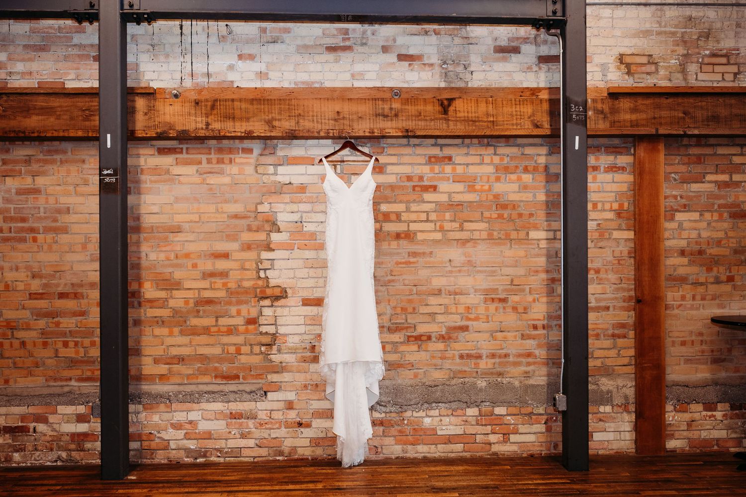 A row of white wedding dresses hanging against exposed brick walls in an industrial-style venue.
