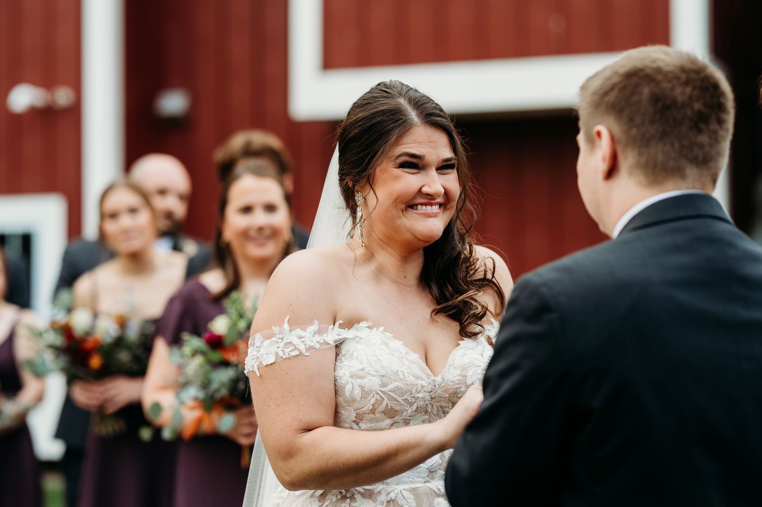 Wedding celebration scene outdoors with guests and couple in front of red barn during autumn ceremony.