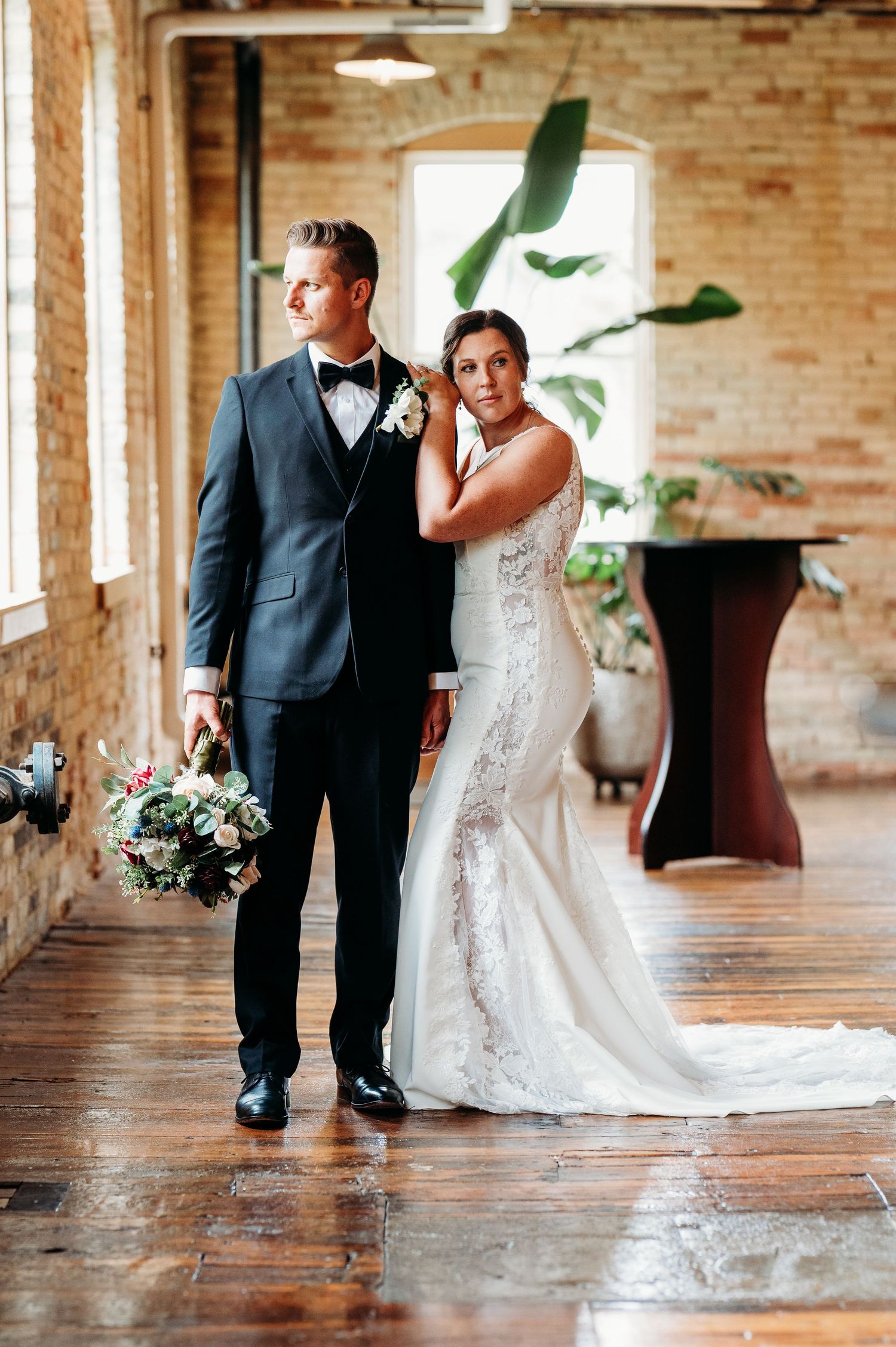 Bride and groom share intimate moments in a rustic industrial venue with exposed brick walls.
